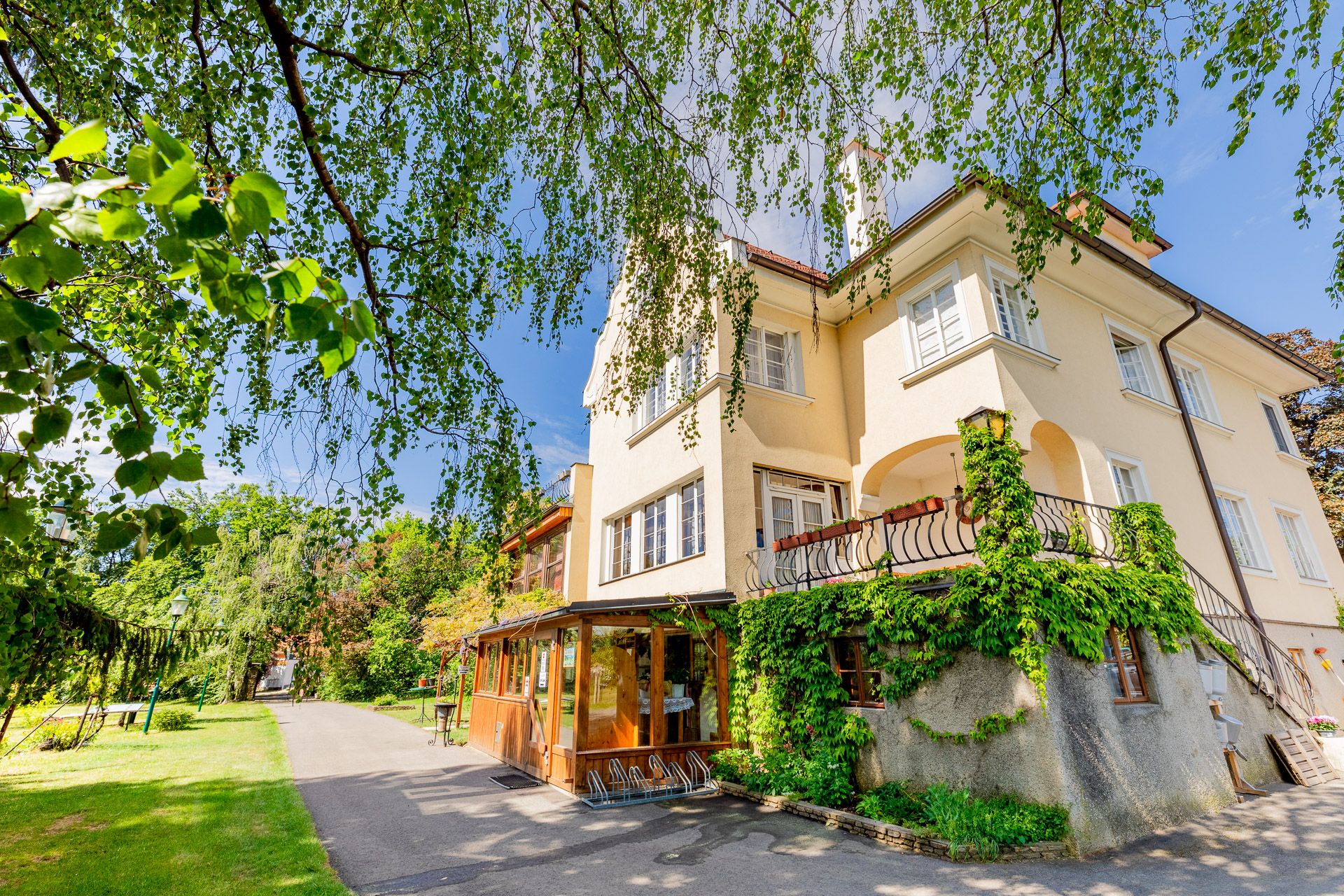 A yellow manor house overgrown with ivy, surrounded by trees and a garden path.