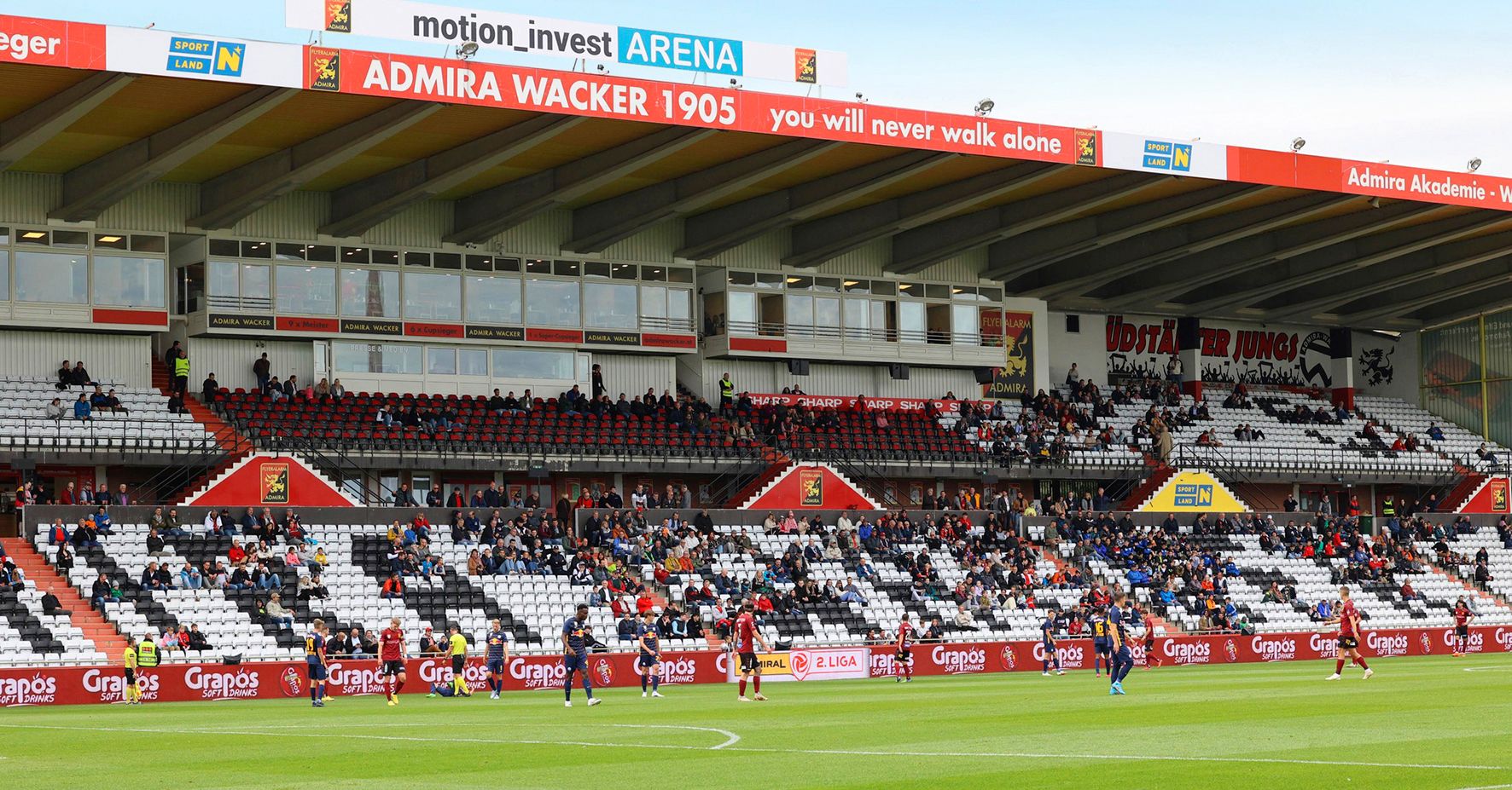 Soccer stadium with spectators in the stands and players on the pitch.