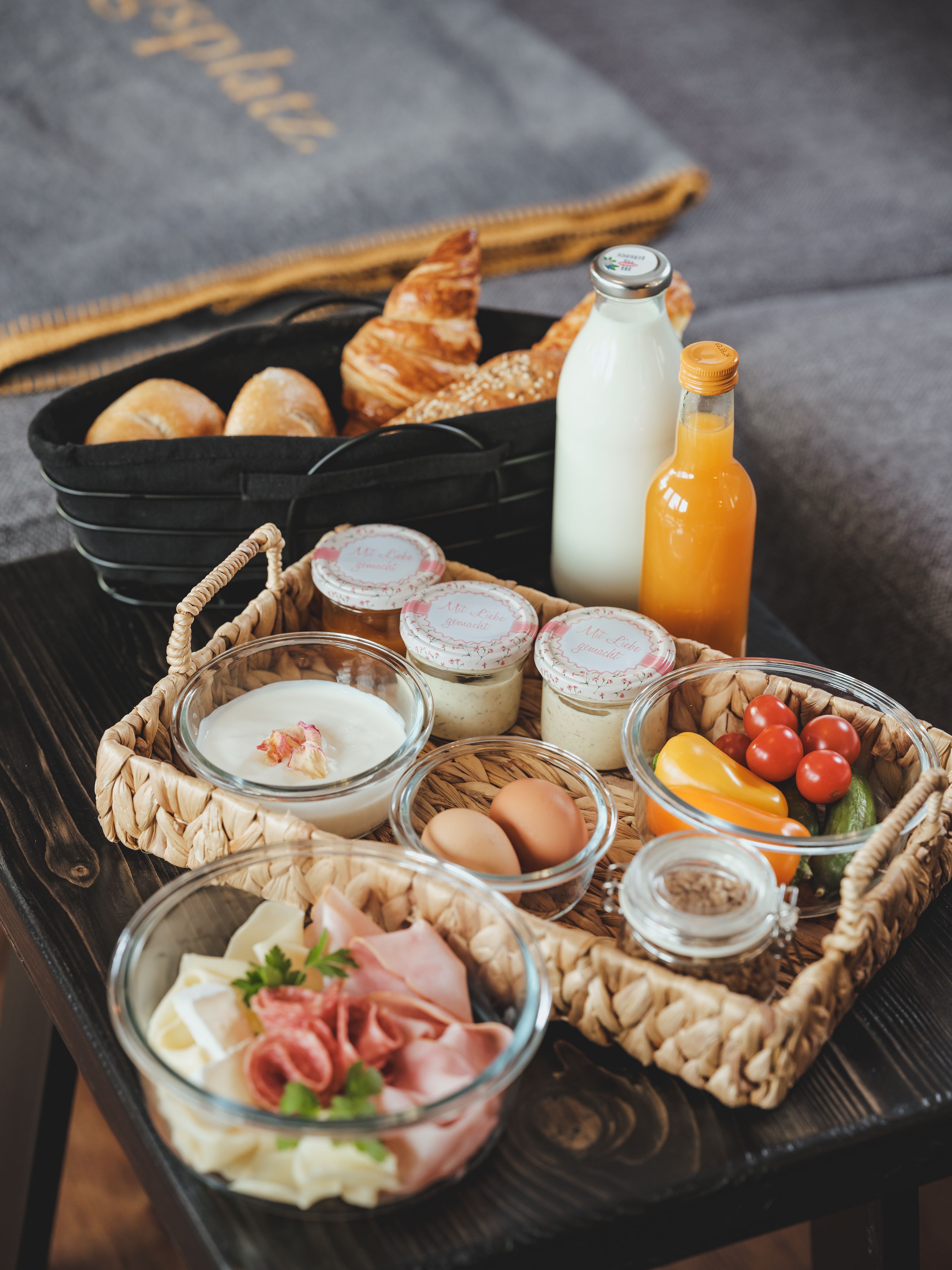 Breakfast tray with bread rolls, croissant, milk, juice, yogurt, eggs, cold cuts and vegetables.
