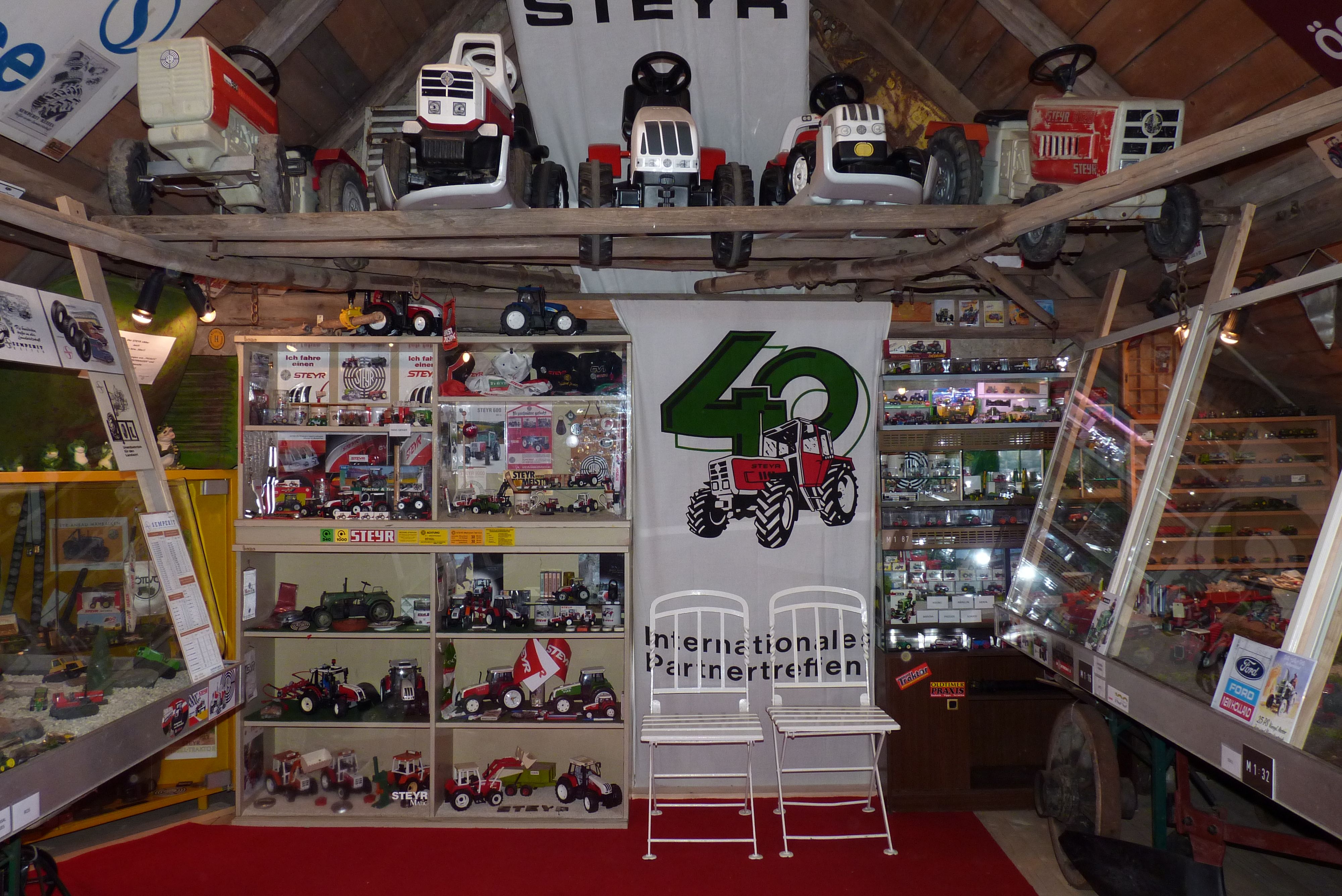 Exhibition of Steyr tractor models and toy tractors in a room with a wooden ceiling.