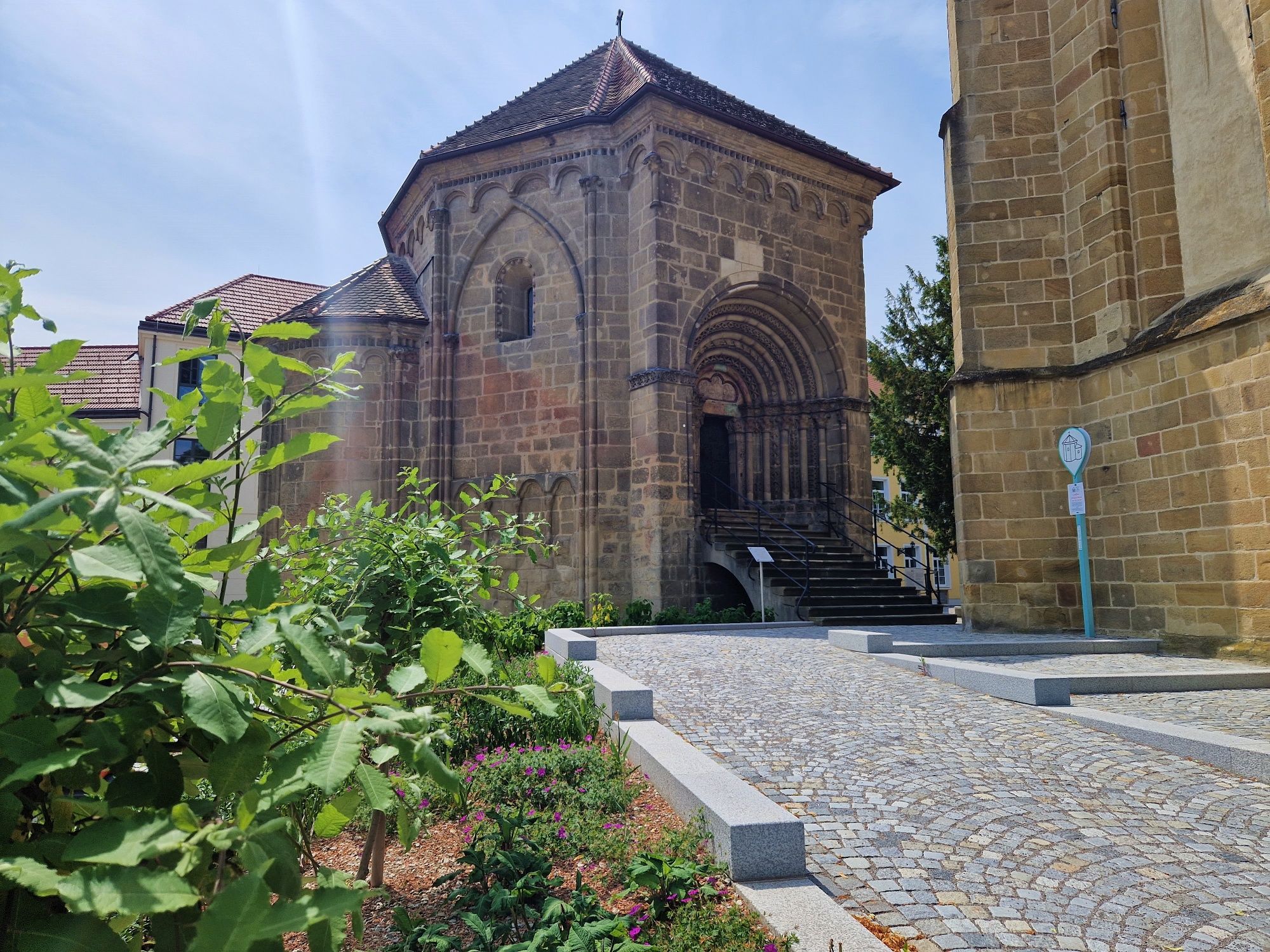 Historic building with Romanesque portal and garden in the foreground.