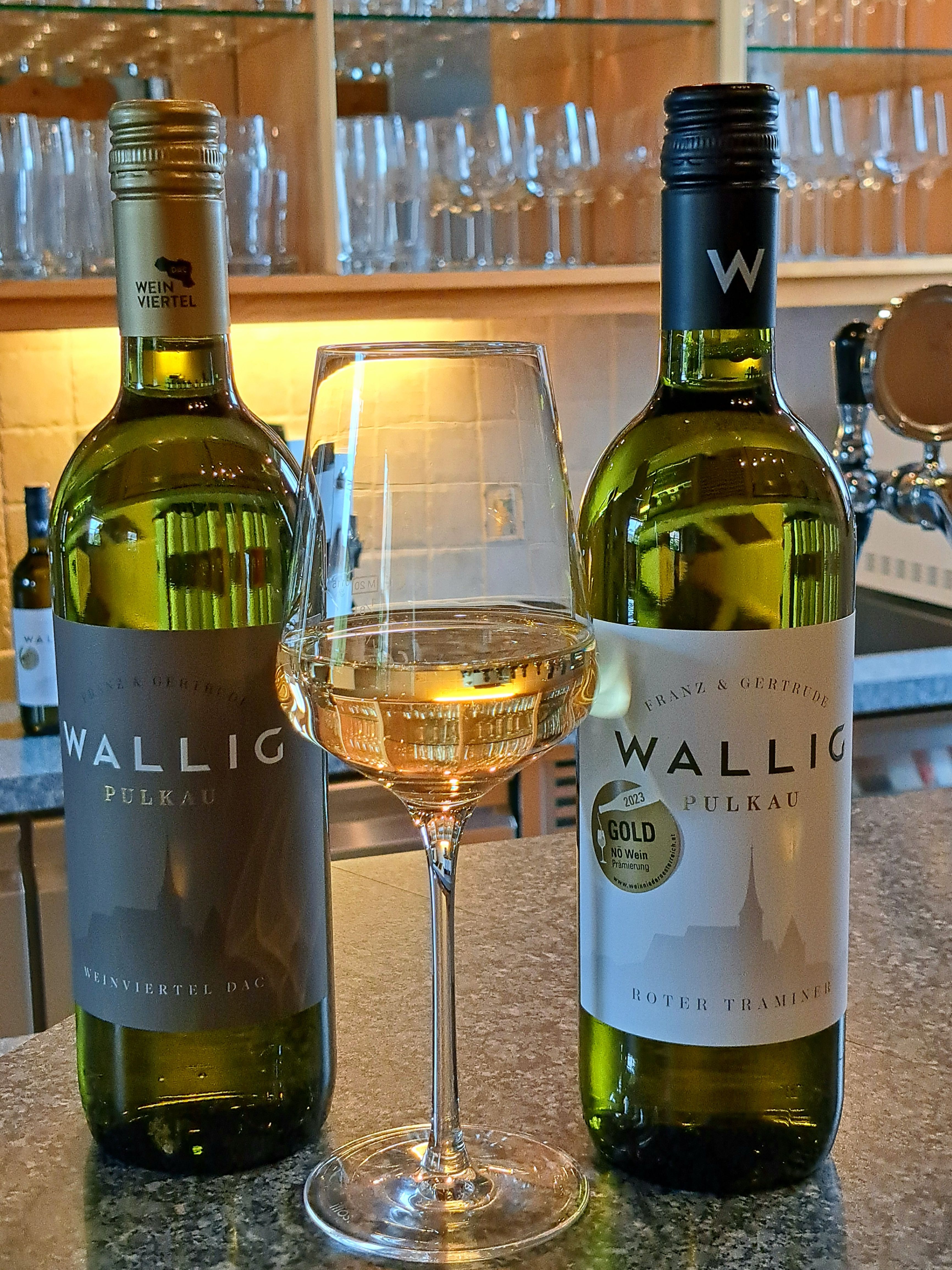 Two bottles of wine and a glass of white wine on a counter.