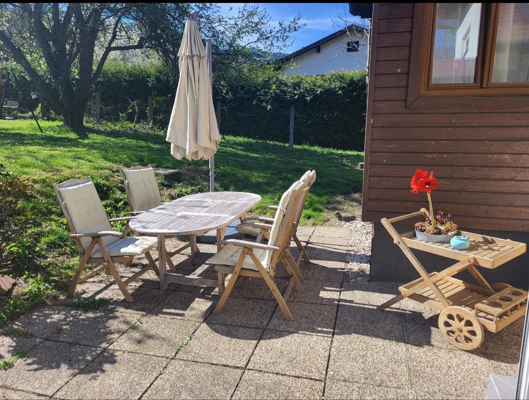 Terrace with wooden furniture and parasol, surrounded by garden.
