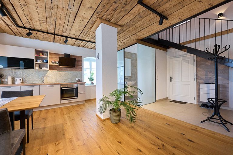 Modern kitchen with wooden floor and ceiling, staircase and plants.