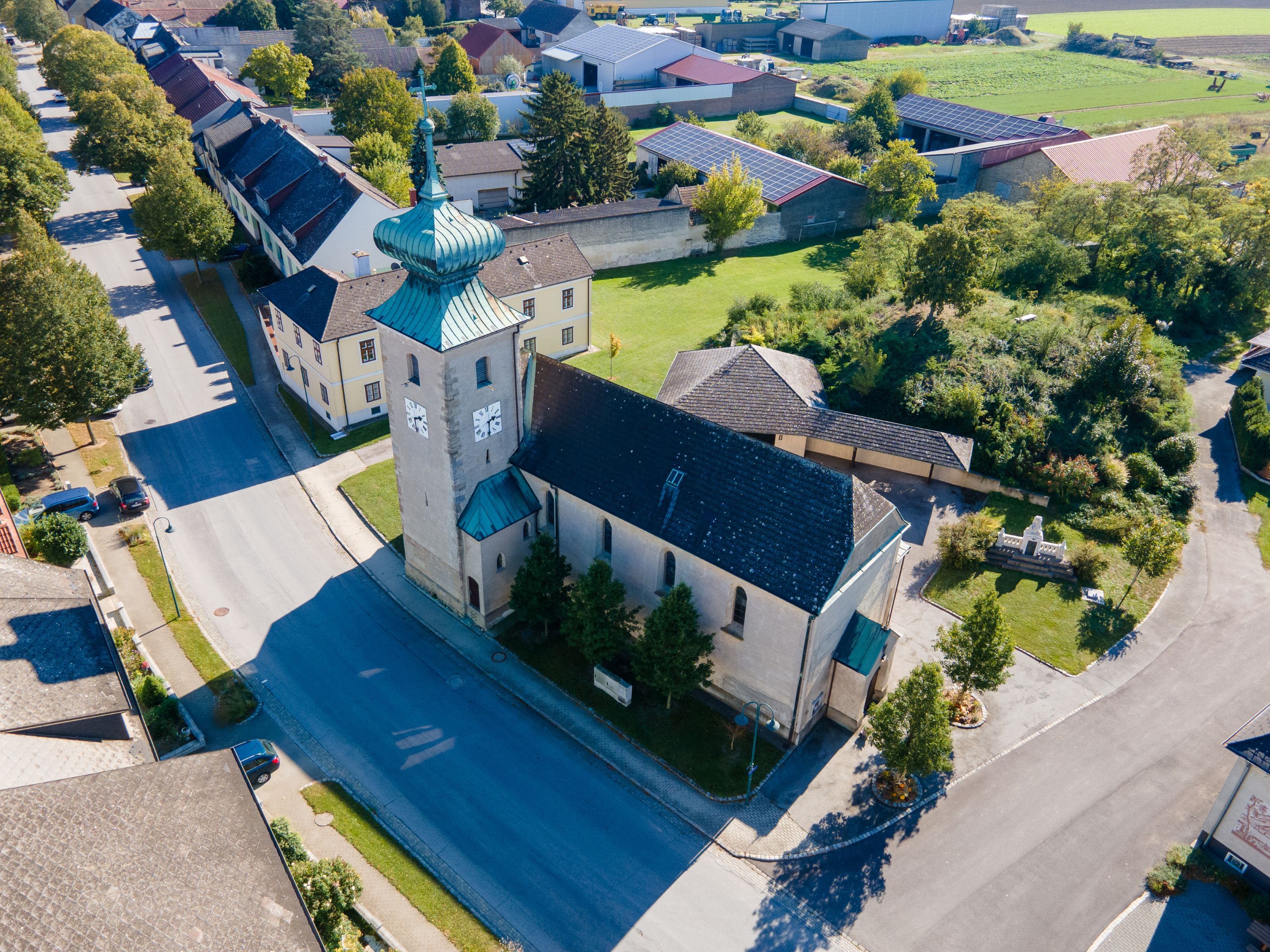 Aerial view of the church in the town of Weiden an der March, showing its tower, copper roof, and the surrounding houses and gardens.