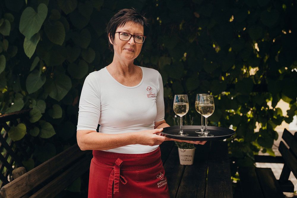 Woman with glasses and tray with two wine glasses outdoors.