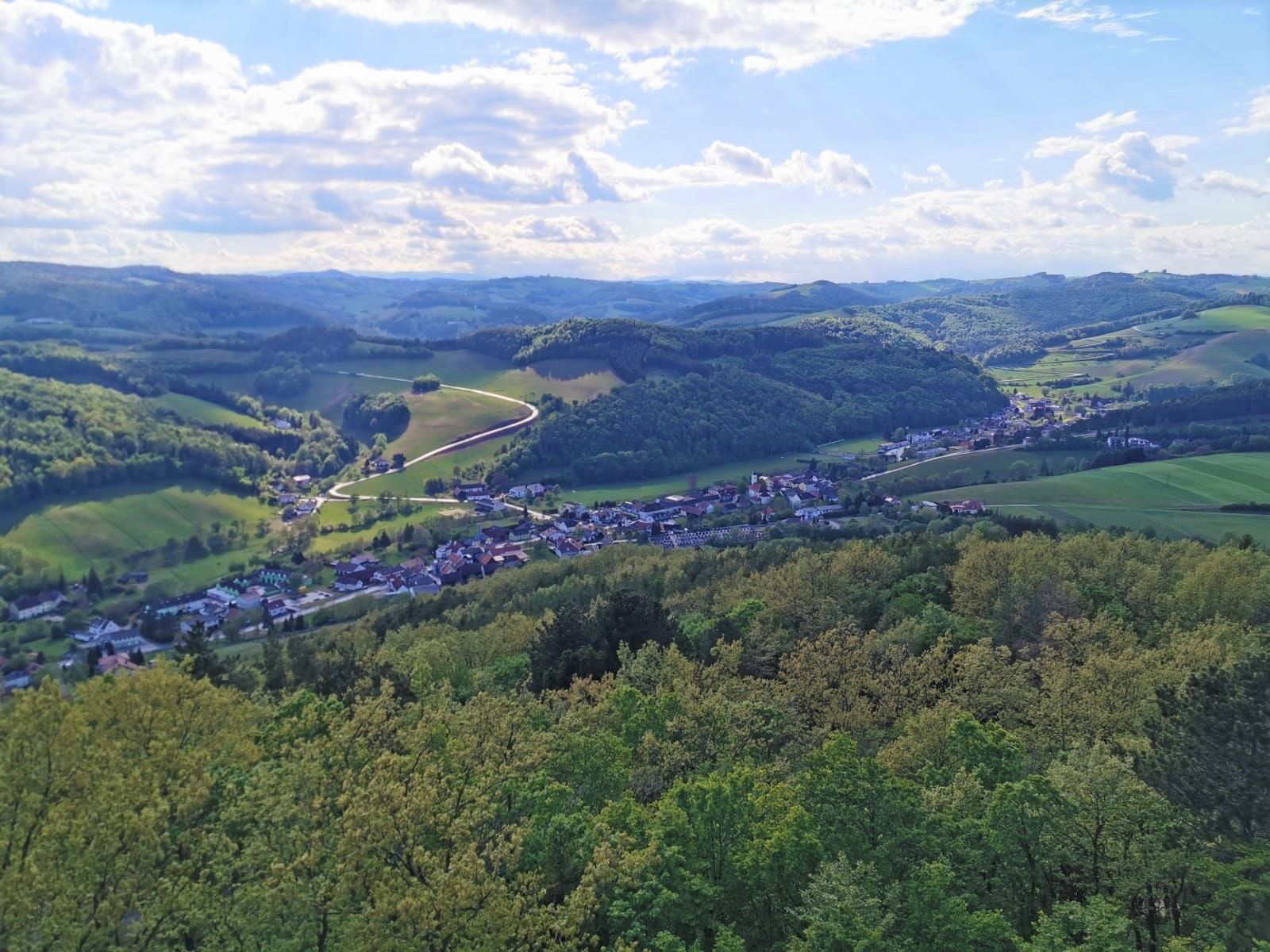 Panoramic view of green hilly landscape with forests, blue sky and small village.