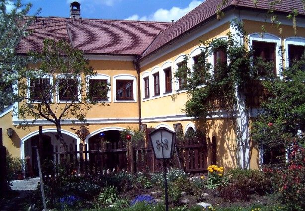 Yellow house with red roof tiles and garden in the foreground.