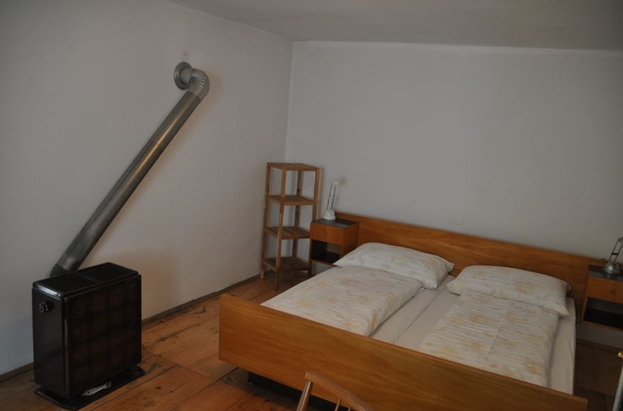 A simply furnished bedroom with double bed, bedside tables, shelf and stove.