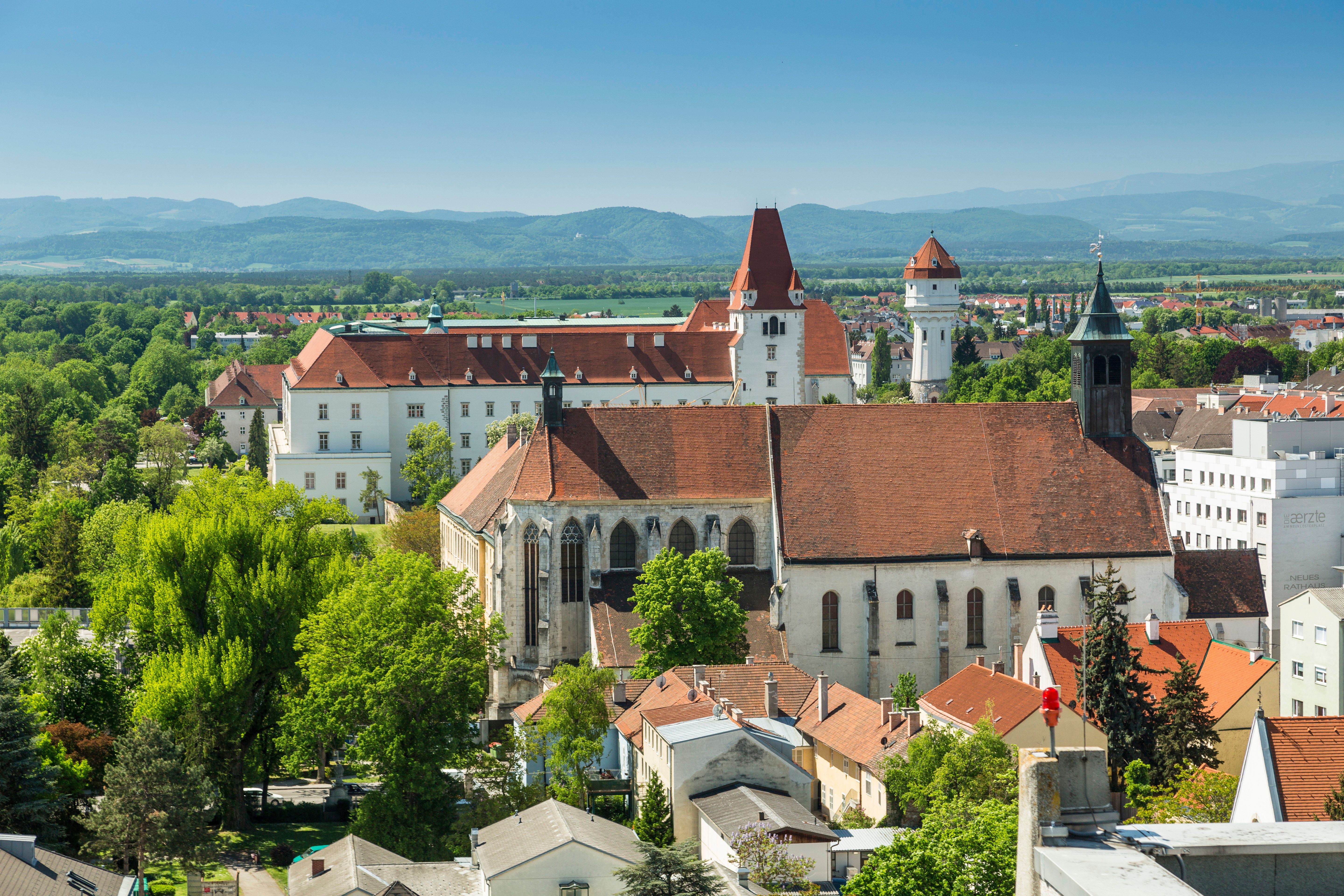 Three landmarks in one photo: Neukloster Abbey, the Theresian Military Academy at Akademiepark, and the water tower. In the background are the mountains of the Vienna Alps.