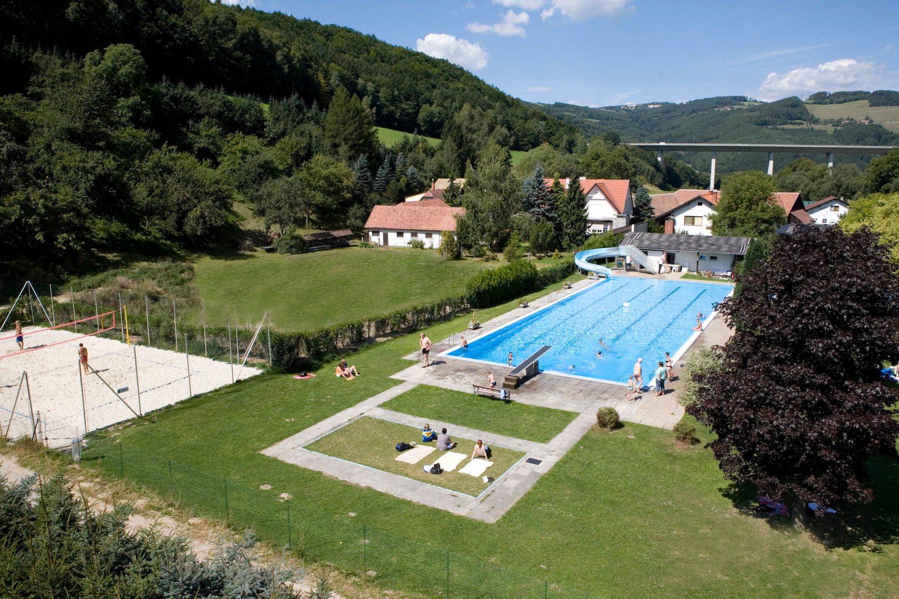 Edlitz outdoor pool with swimming pool, slide and volleyball court in a rural setting.