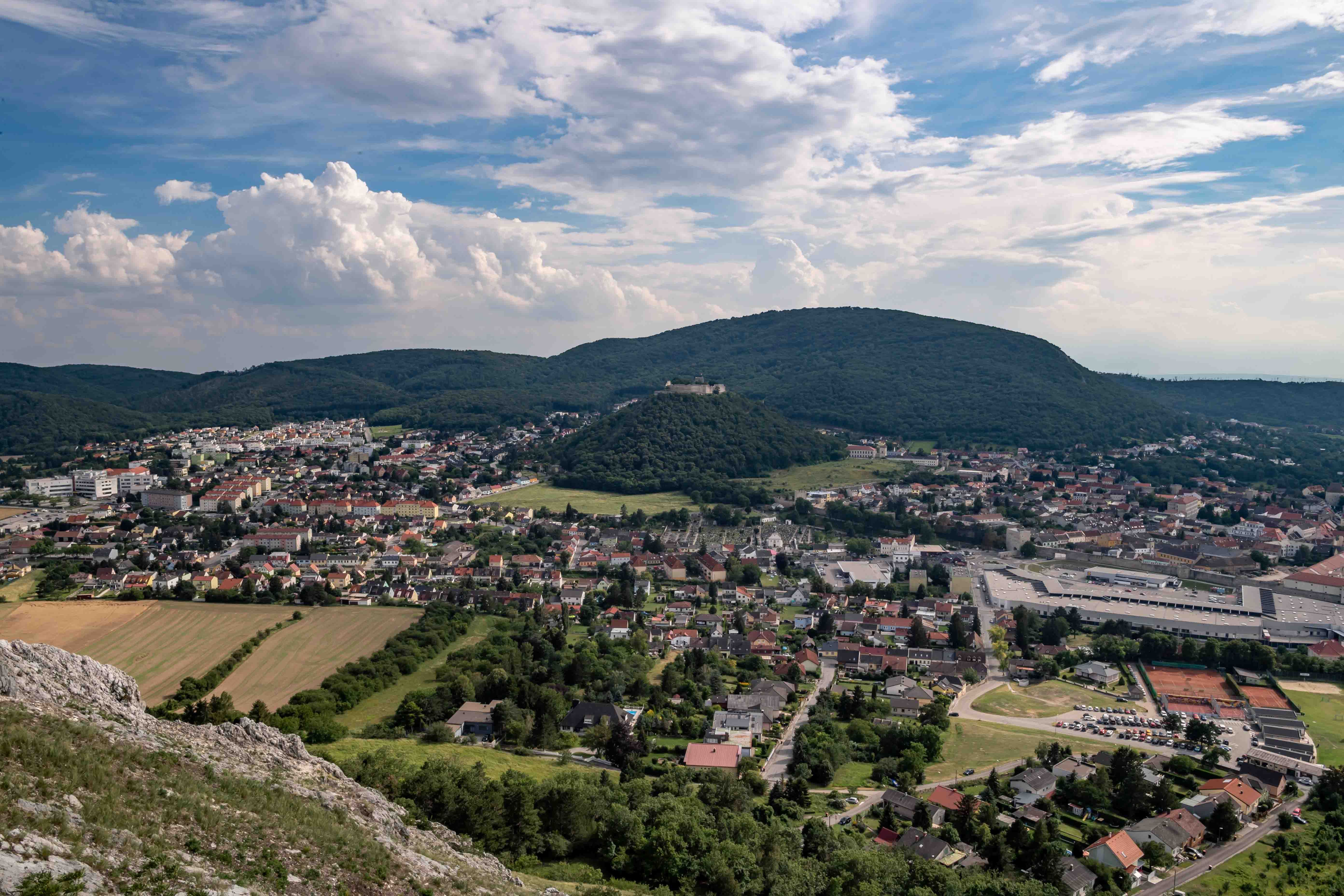 Panoramic view of a city with hills in the background and a cloudy sky.