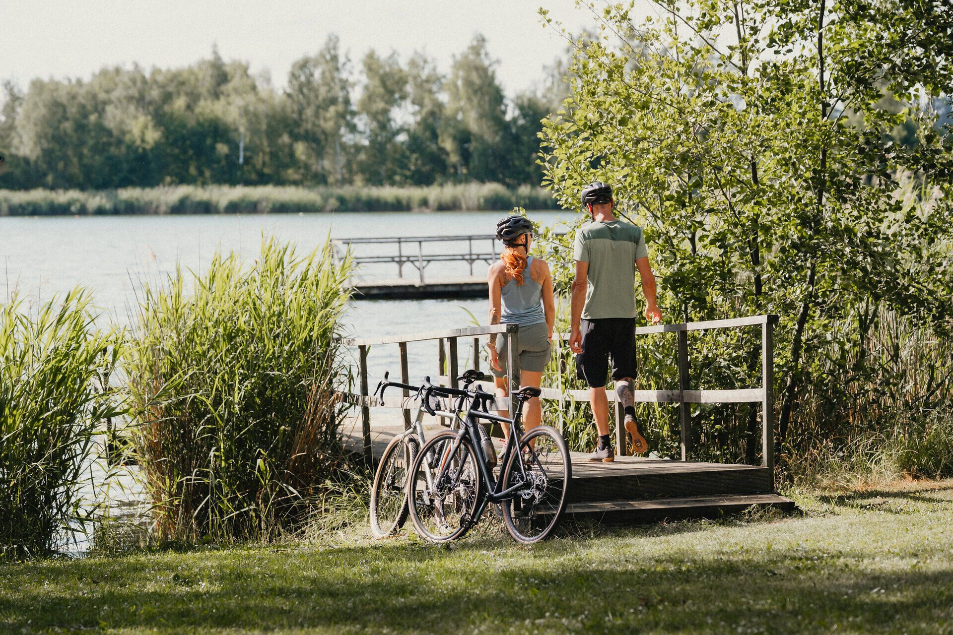 Two people are walking towards the Bergwerksee lake along a footbridge, having parked their bikes beforehand
