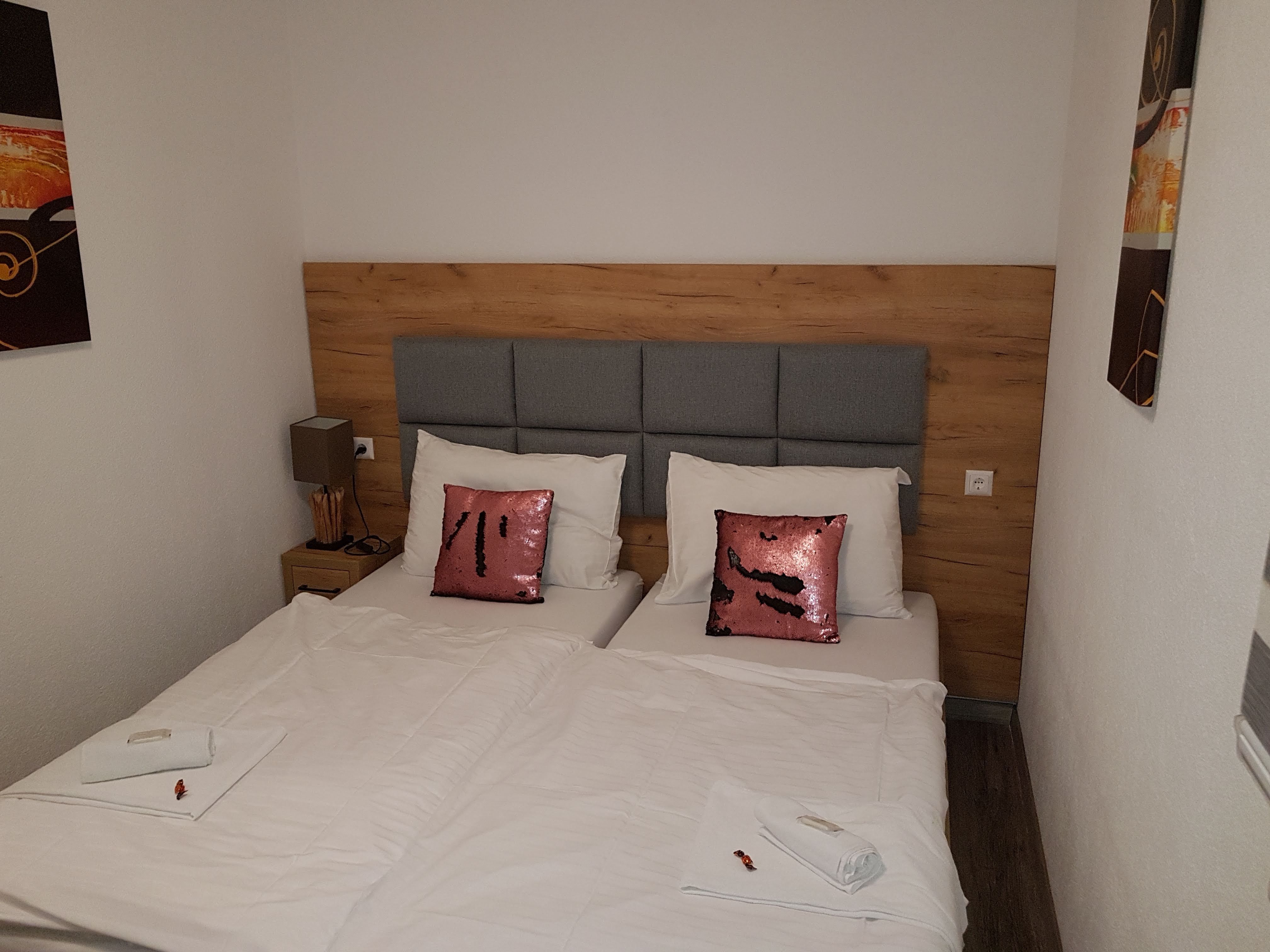 Double room with two single beds, gray headboard, pink sequin pillows and white bed linen.