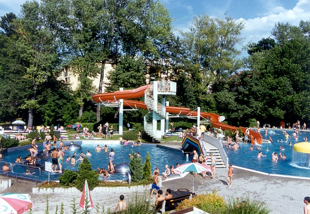 An outdoor pool with lots of people, a water slide and trees in the background.