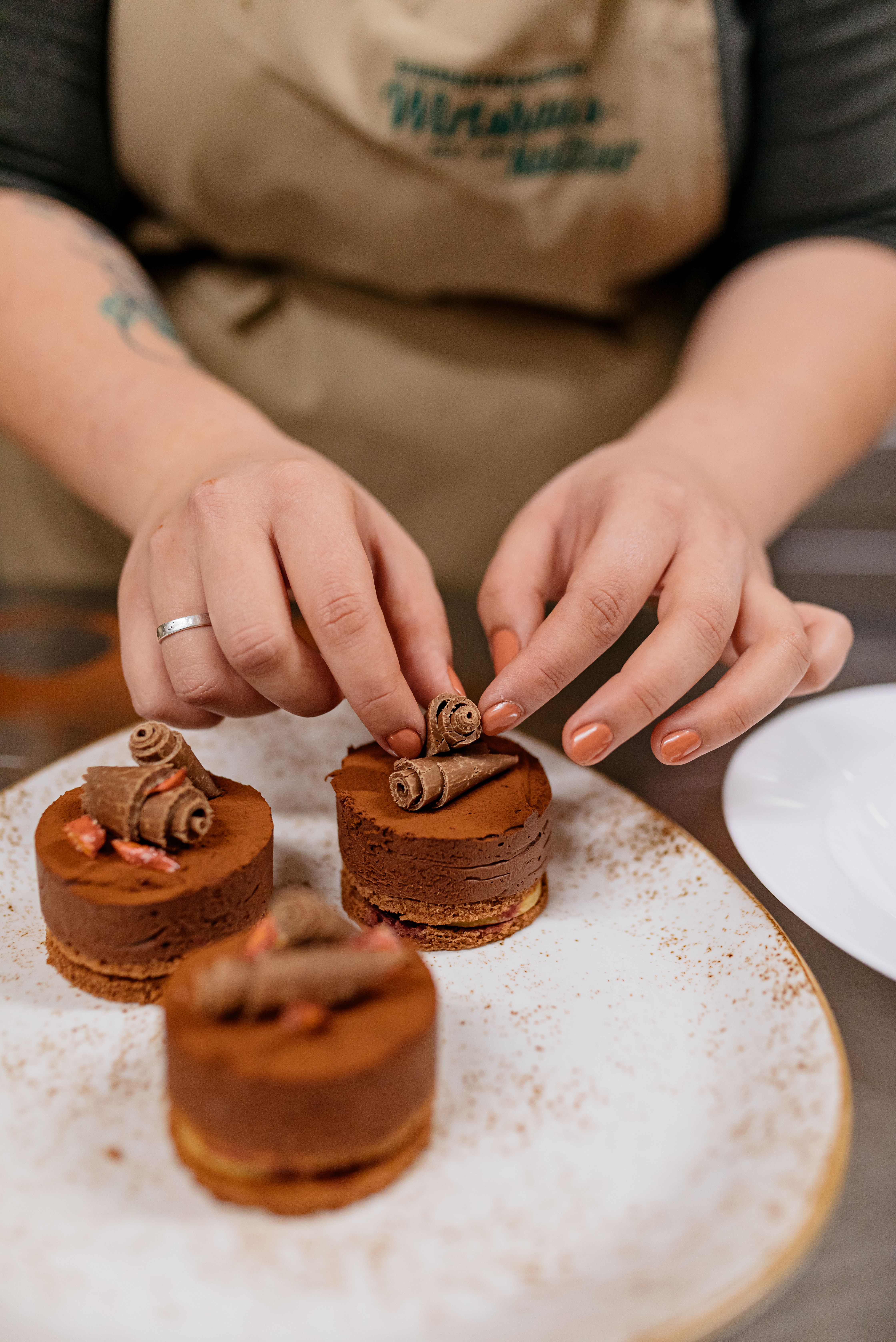 Close-up of a hand with a tattoo decorating chocolate on a plate.