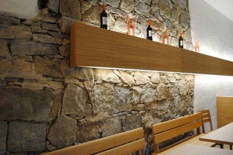 Stone wall with wooden shelf and wine bottles.