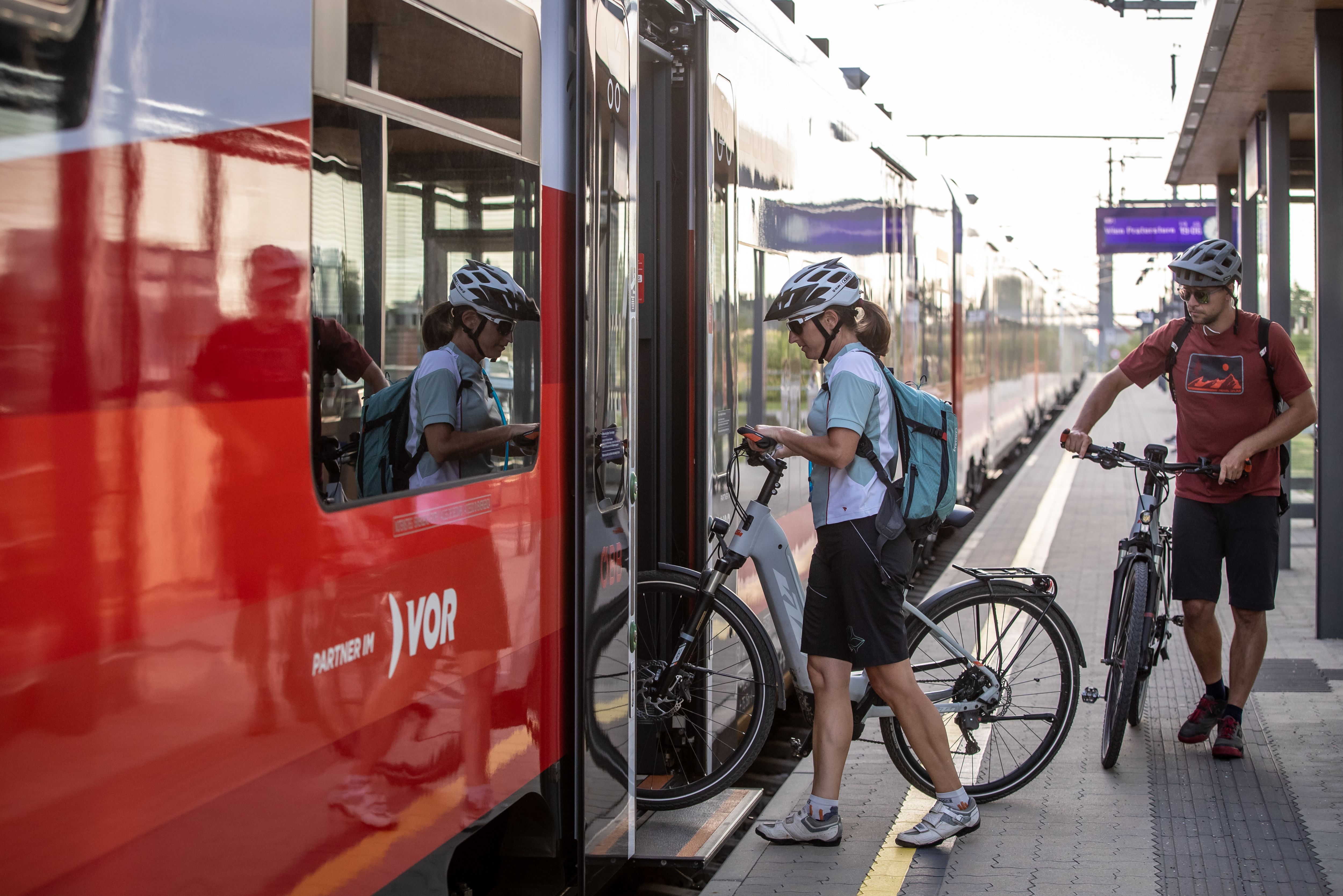Two cyclists get on a train with their bicycles.