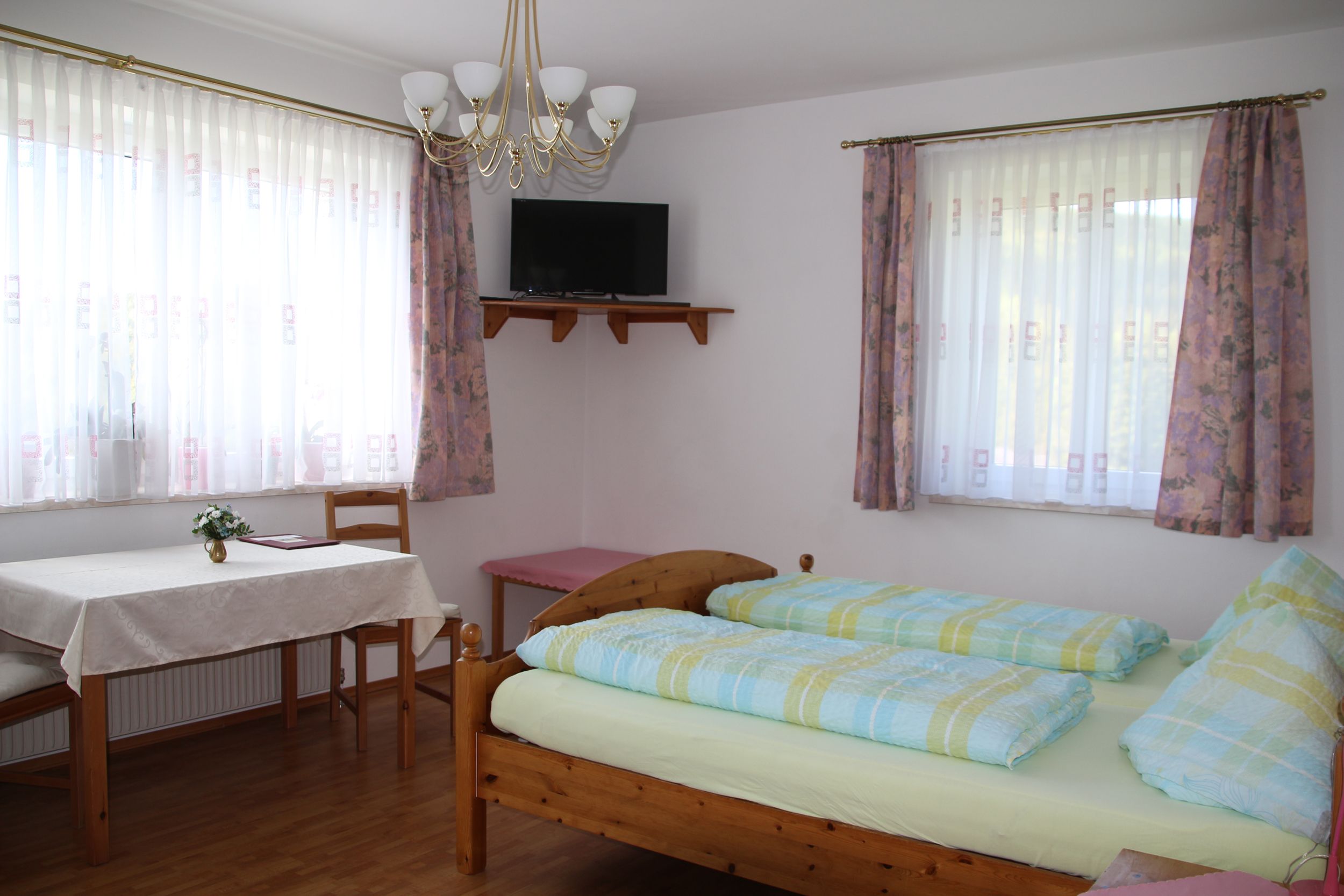 A bright room with a double bed, table, chairs and a TV on the wall.