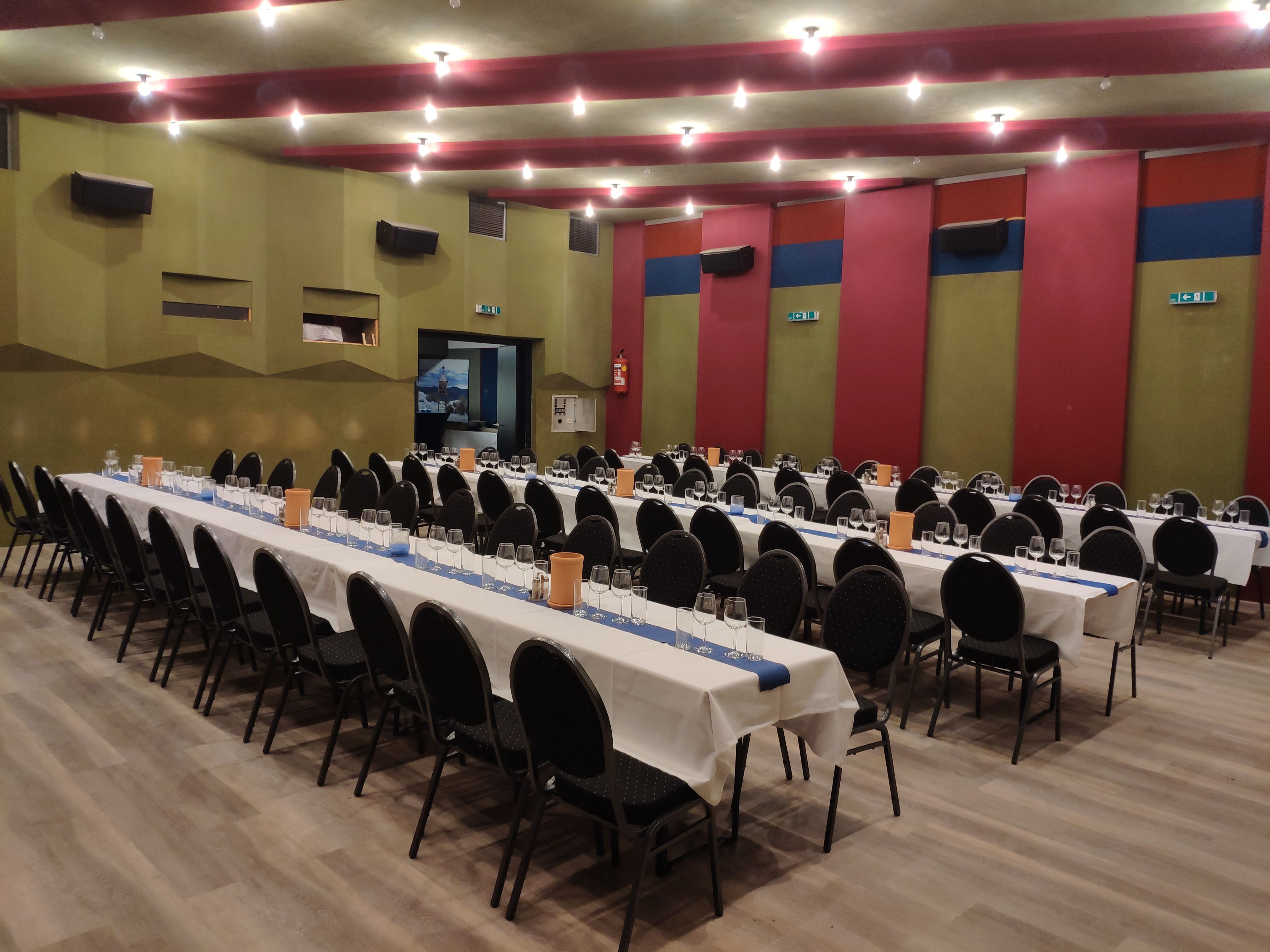 A large hall with long, laid tables and black chairs, ready for an event.
