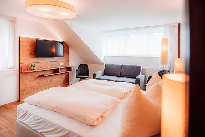 Modern hotel room with double bed, sofa, TV and stylish lighting.