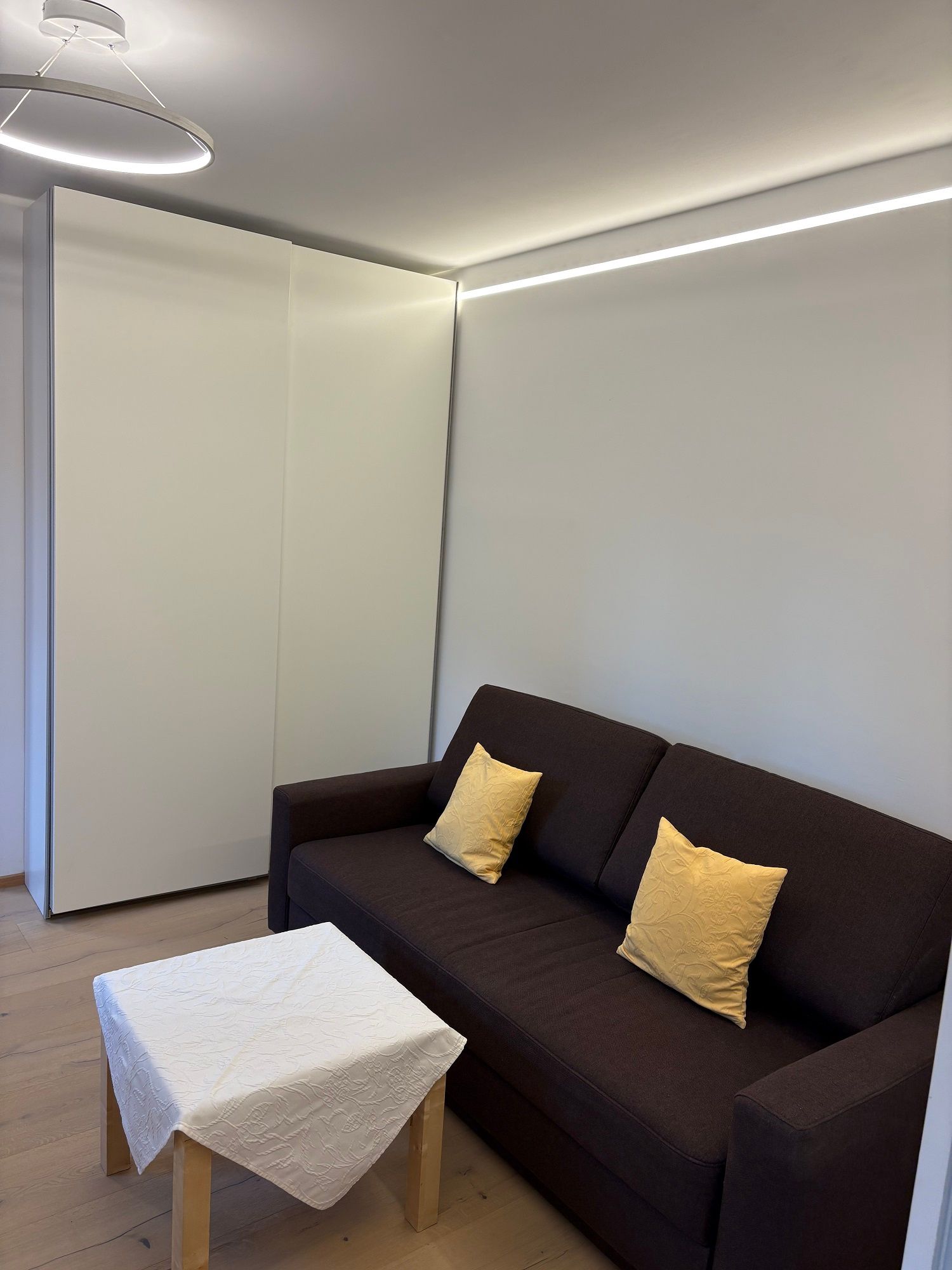 Modern living room with brown sofa, yellow cushions and small table with white tablecloth.
