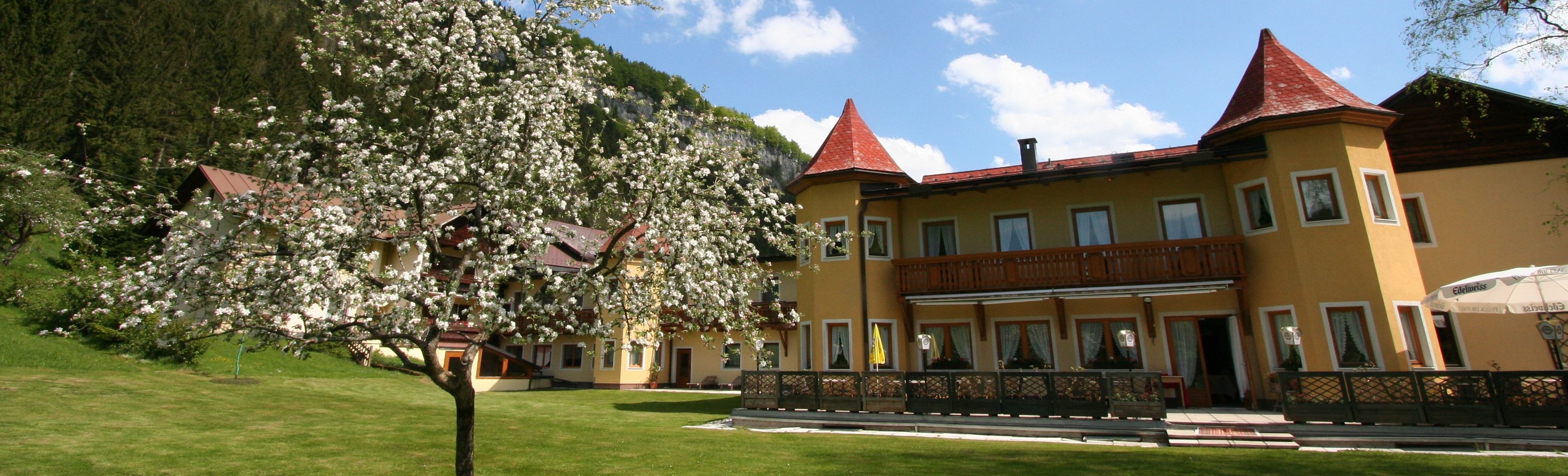 A yellow hotel with red roofs and a blossoming tree in the foreground.