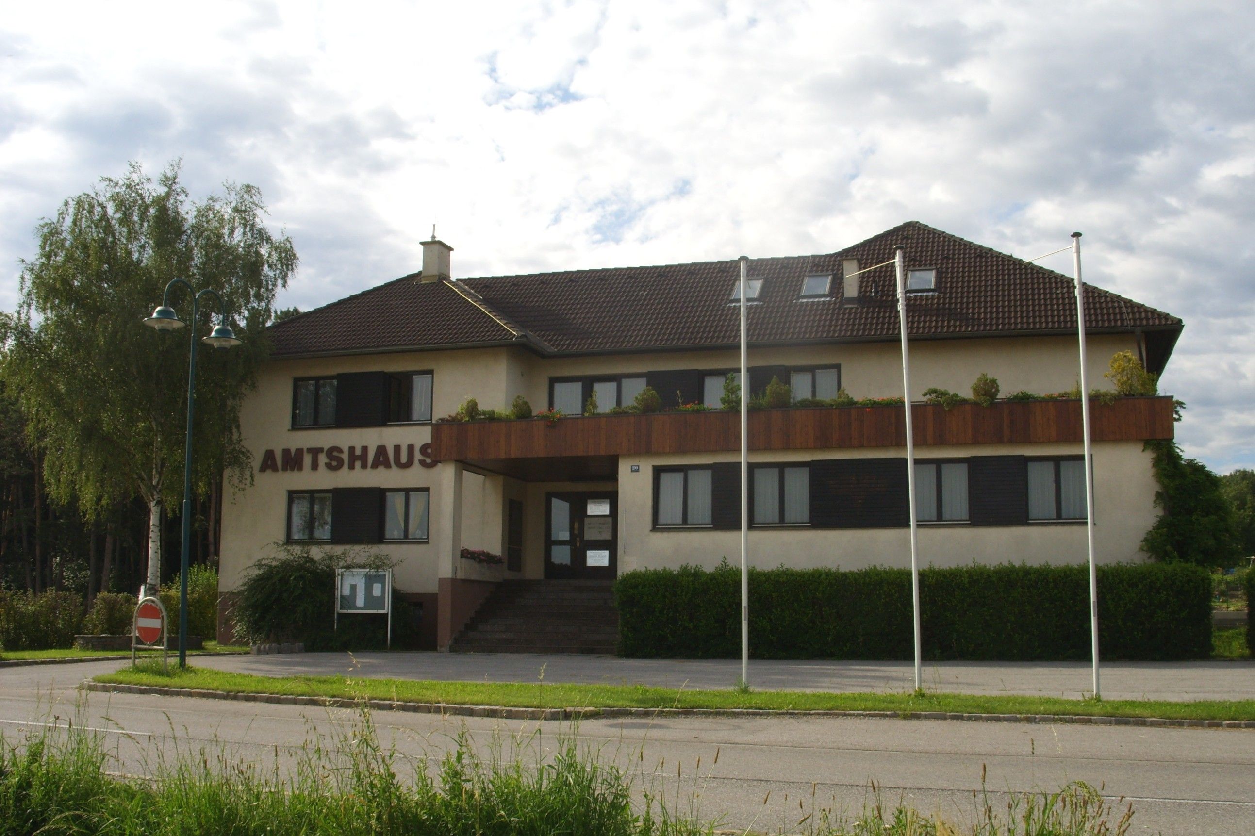 The Natschbach-Loipersbach office building with brown roof and balcony, surrounded by trees and flagpoles.