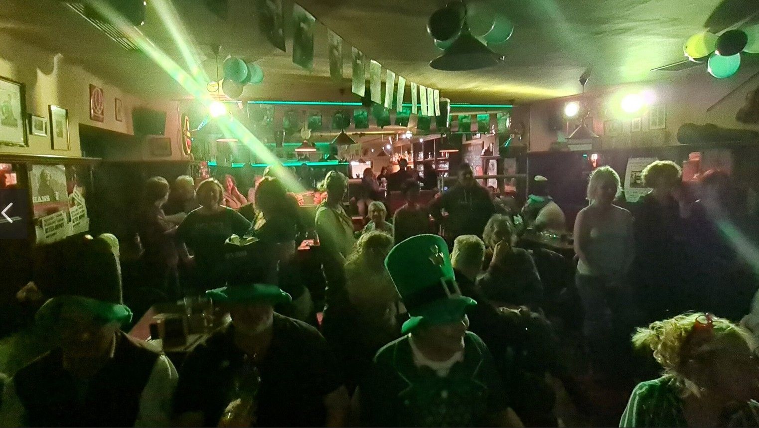 People celebrate in a pub with green decorations and hats on St. Patrick's Day.