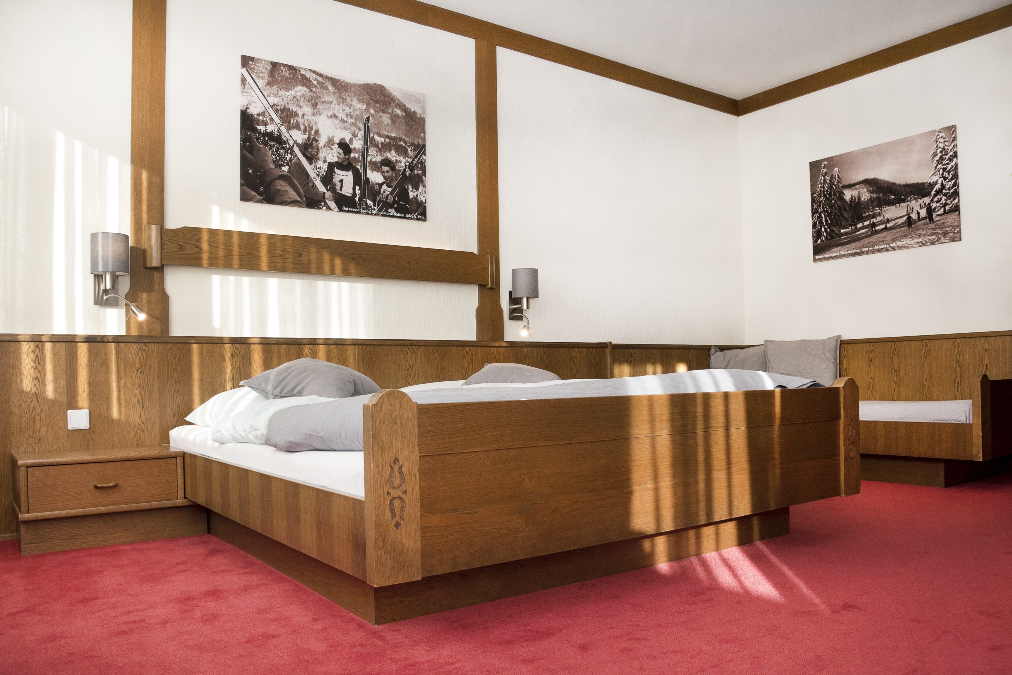 A bedroom with a wooden double bed, red carpeting and two black and white pictures on the wall.