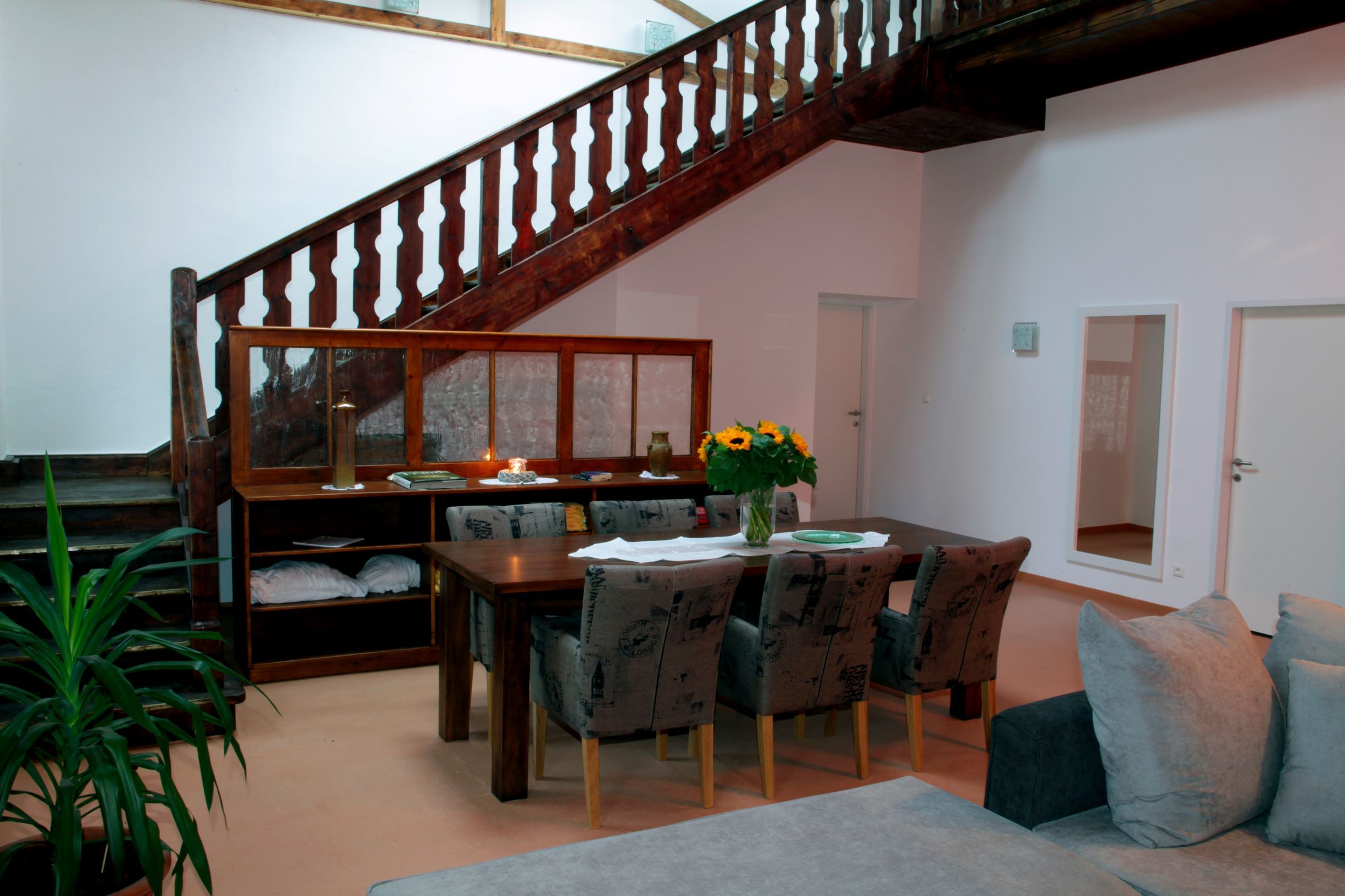 Dining area in a loft with wooden table, chairs, stairs and plants.