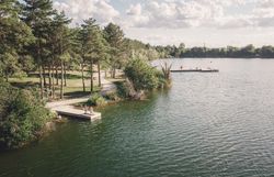 Blick aus der Vogelperspektive über den Viehofner See in St. Pölten mit bewaldetem Ufer, Wegen und mehreren Badestegen; auf einem Steg entspannen zwei Personen.