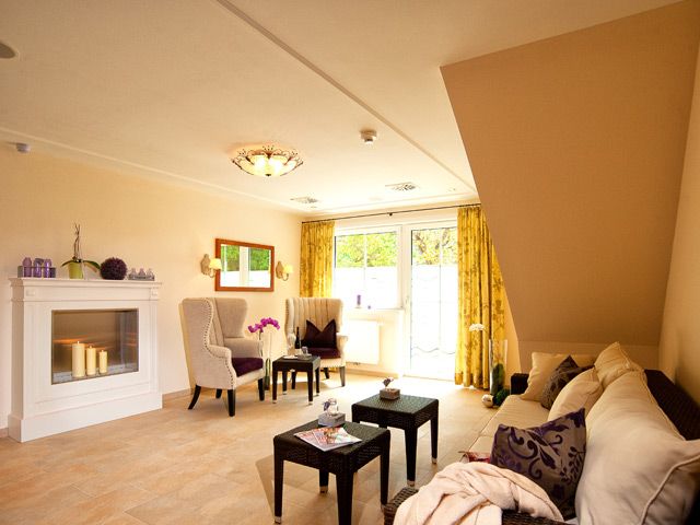 A cozy wellness relaxation area with fireplace, armchairs, sofa and small table, decorated with candles and plants.