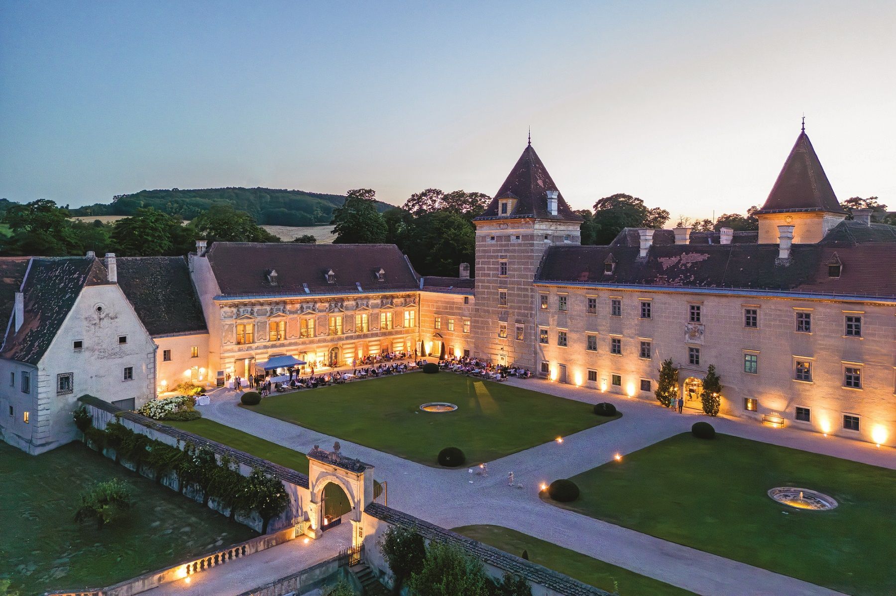 Aerial view of Walpersdorf Castle at dusk, illuminated with guests at a garden party in the courtyard.