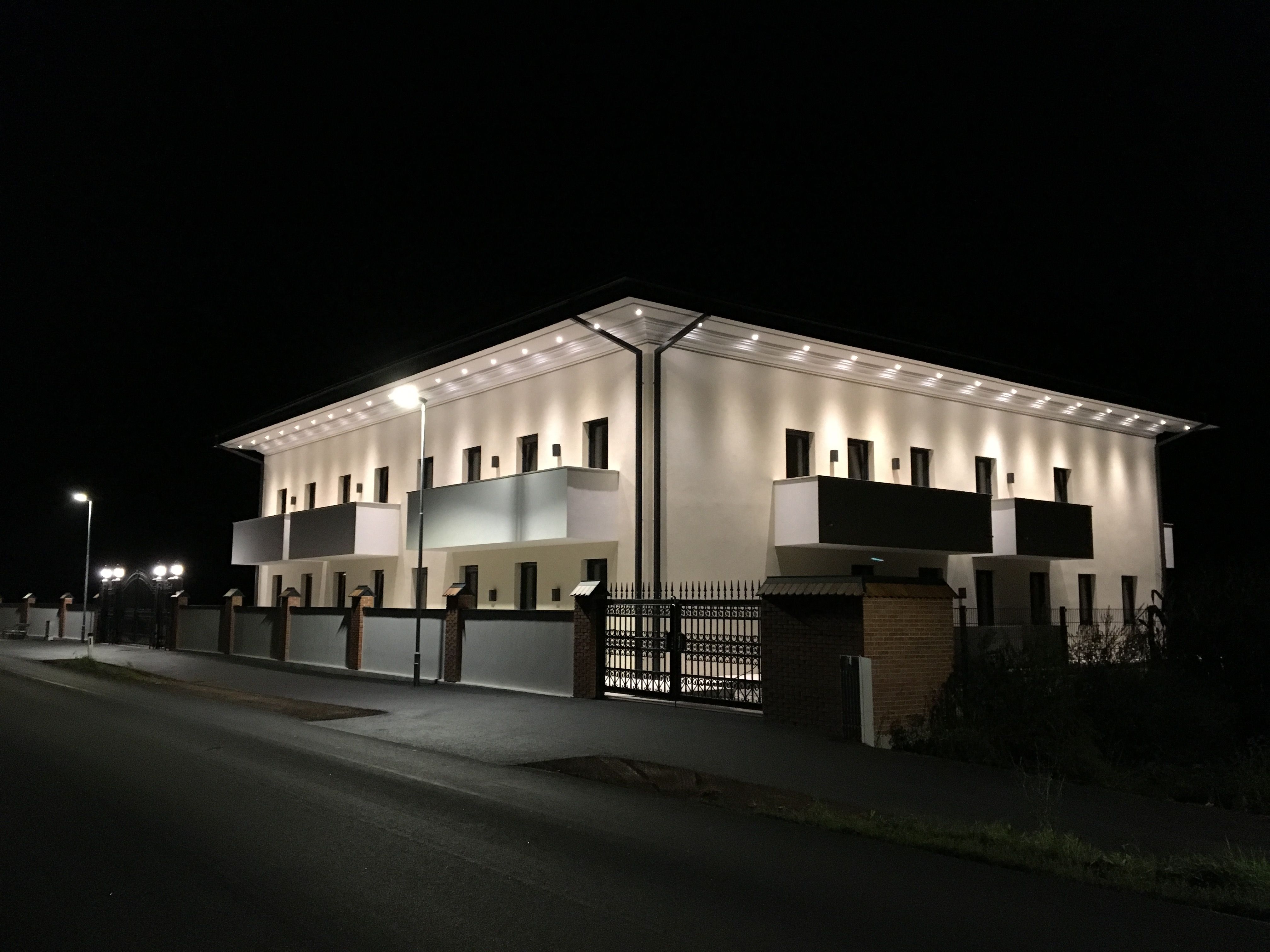 Illuminated building at night with balconies and streetlights.