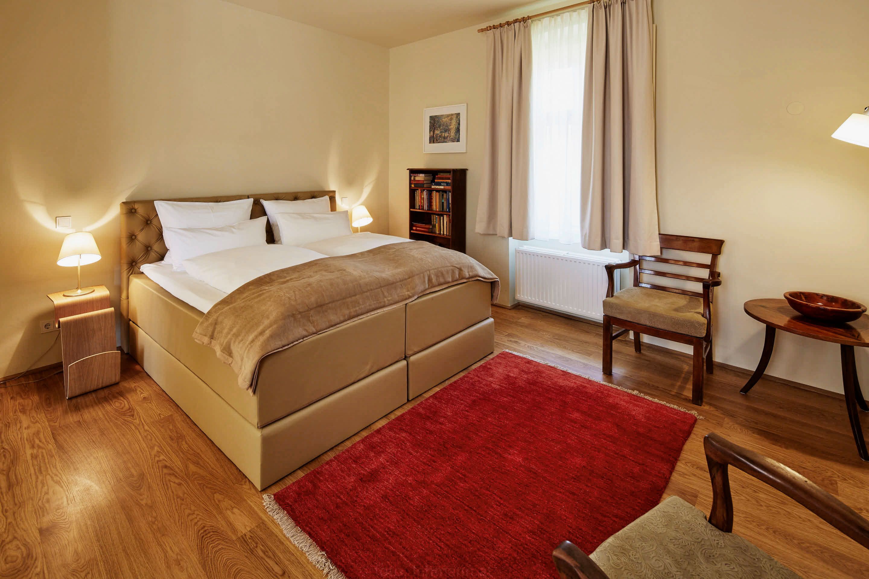 A cozy bedroom with a large bed, two bedside tables with lamps, a red carpet and wooden furniture.