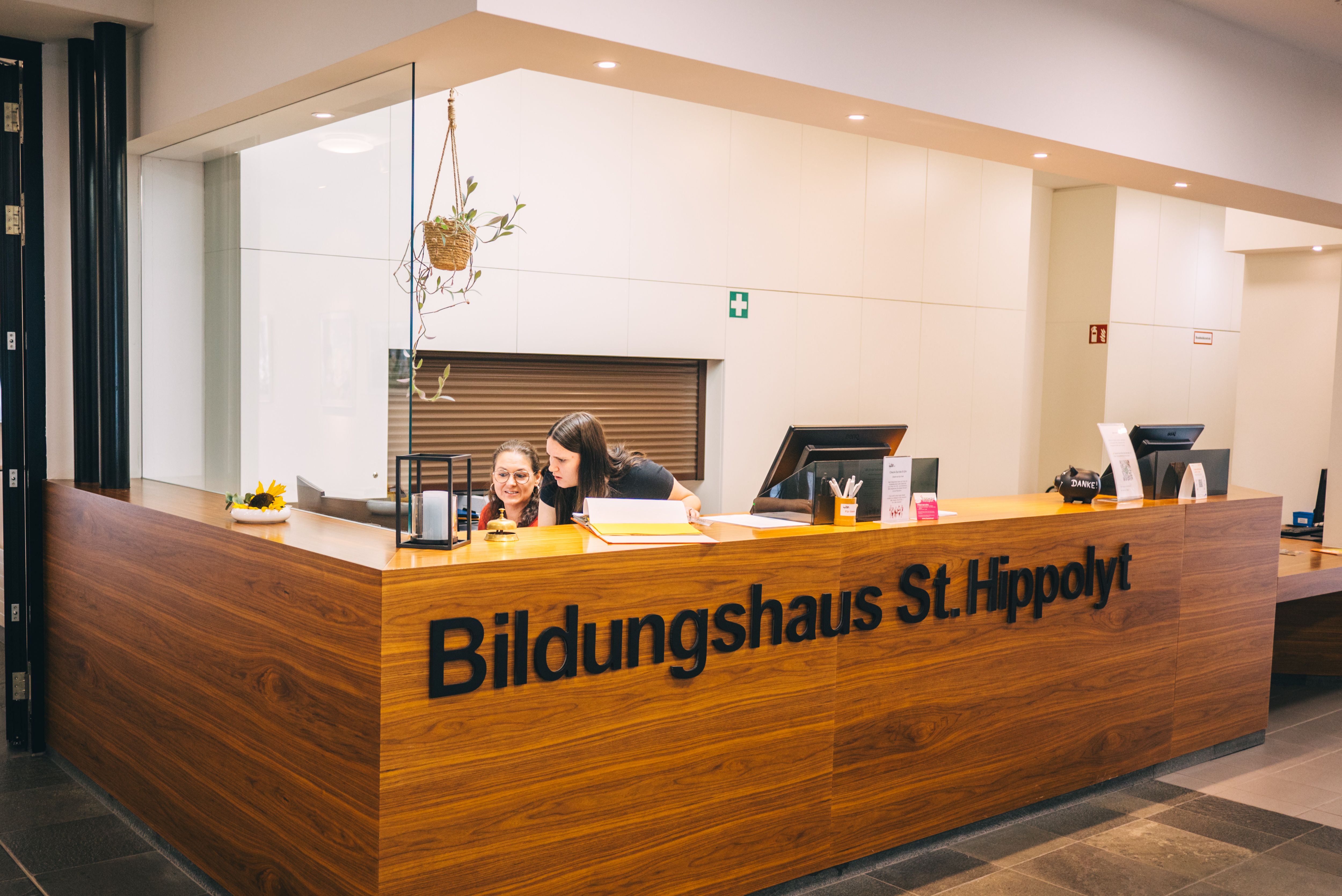 Reception in the St. Hippolyt House of Education with two people behind a wooden counter.