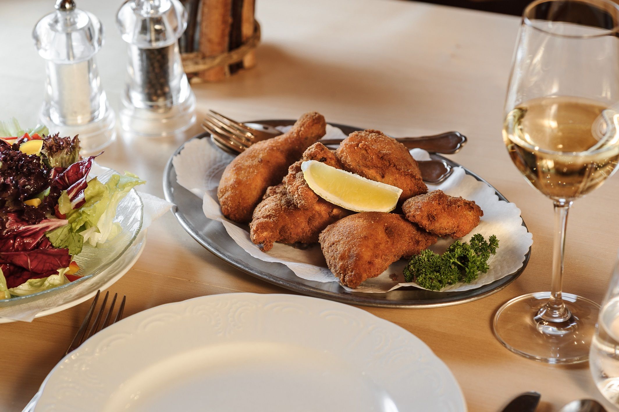 A plate of breaded chicken, salad and a glass of white wine on a table.