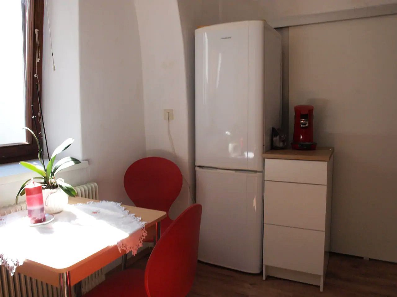 Small kitchen with table, red chairs, fridge and coffee machine.