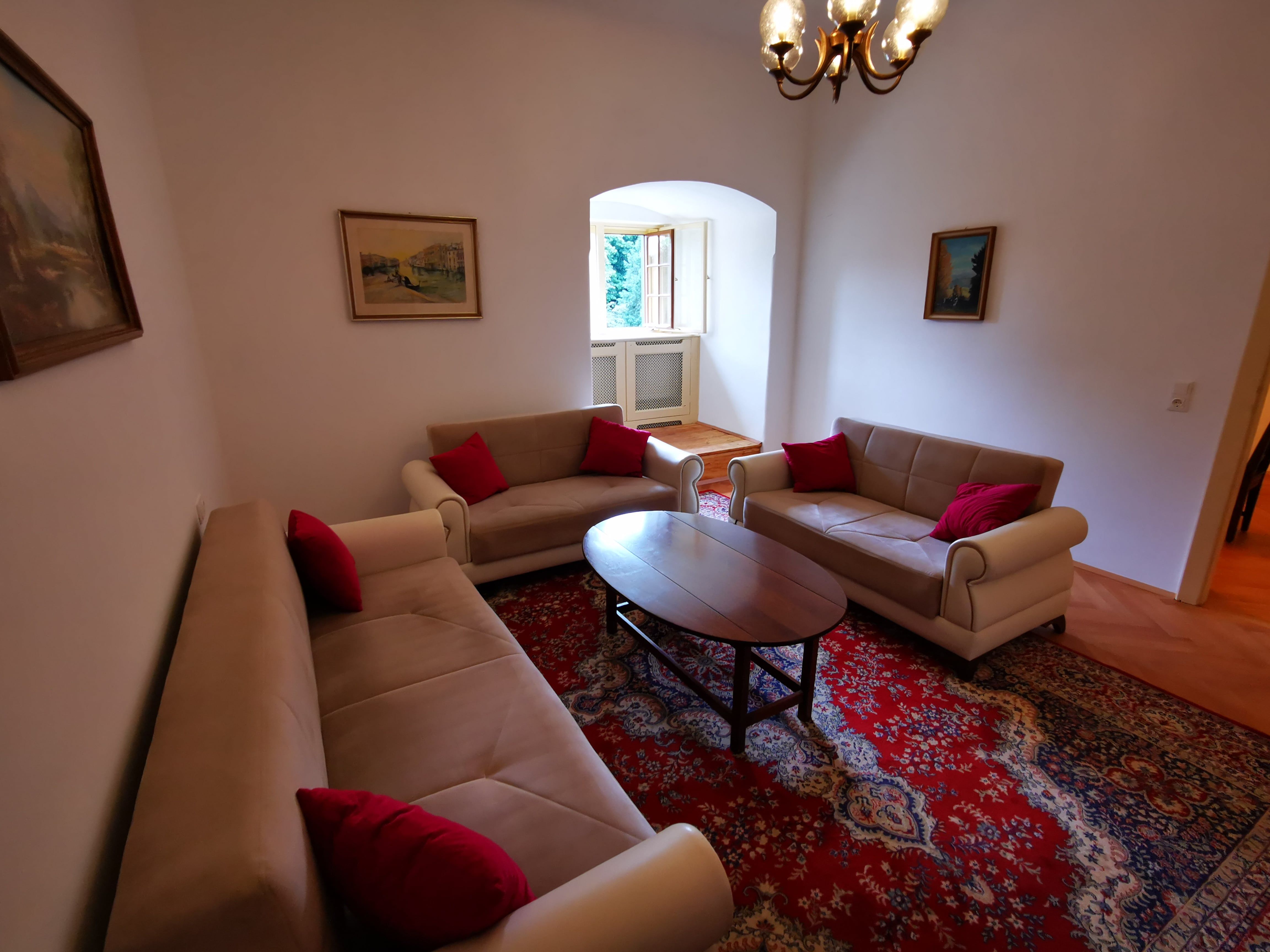 Living room with three sofas, red carpet and paintings on the walls.