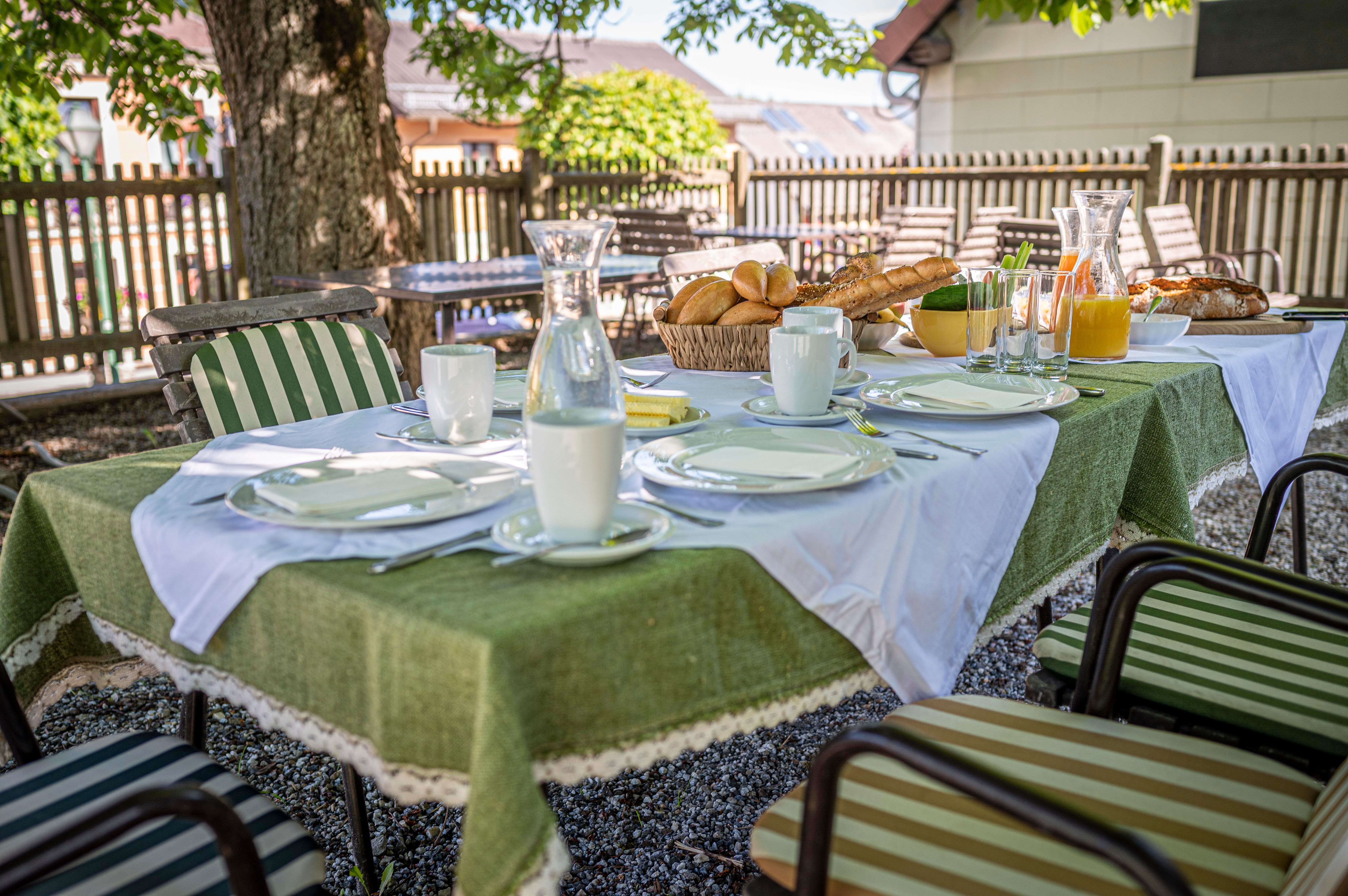 A table laid outside with crockery, bread, juice and milk under a tree.