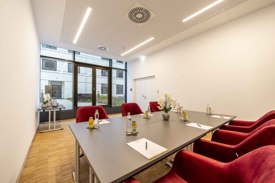 Bright seminar room with wooden floor, terrace, table grouping with red fabric chairs in the middle of the room