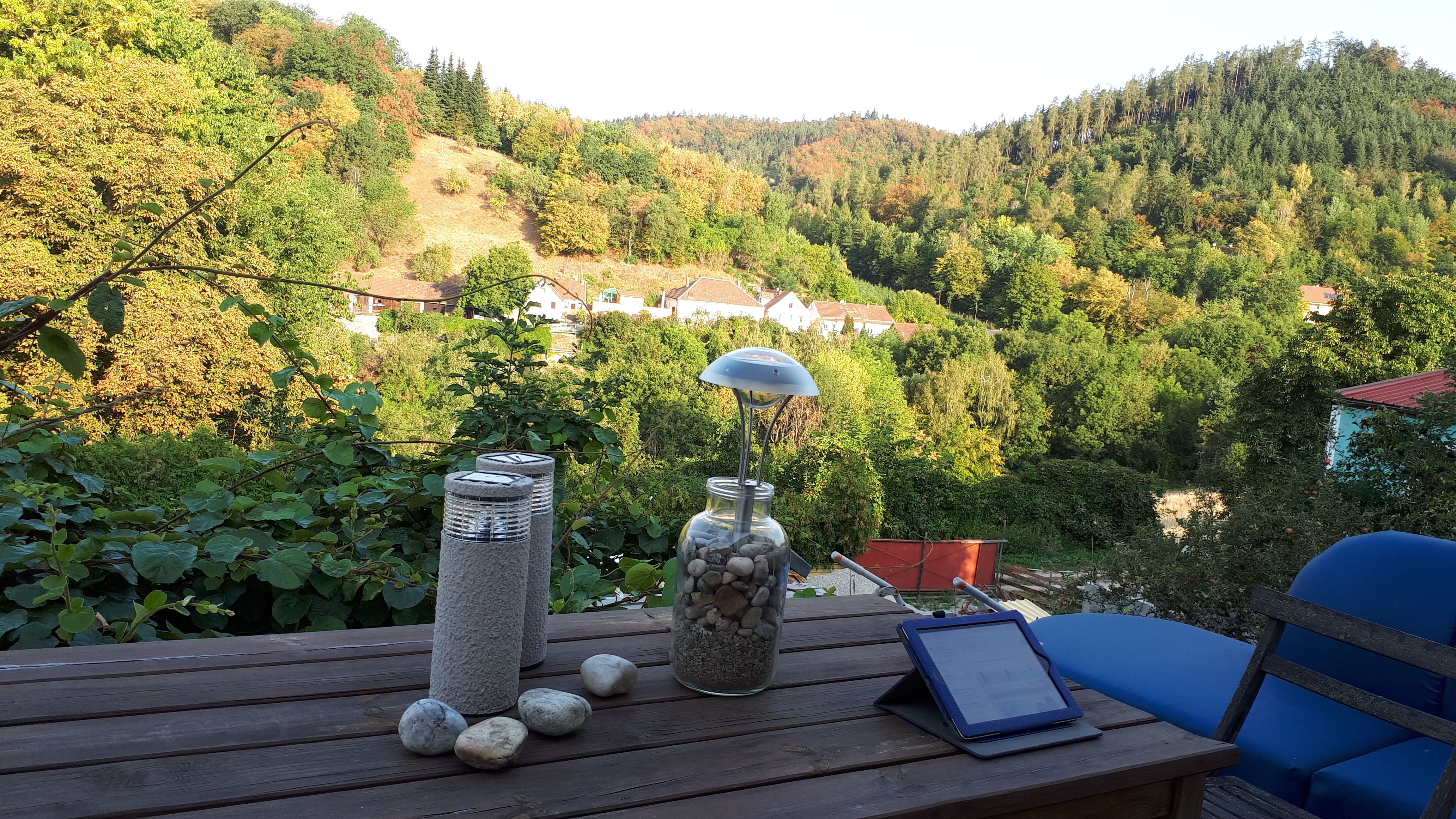 Terrace with table, decoration and view of wooded hills and houses in the background.