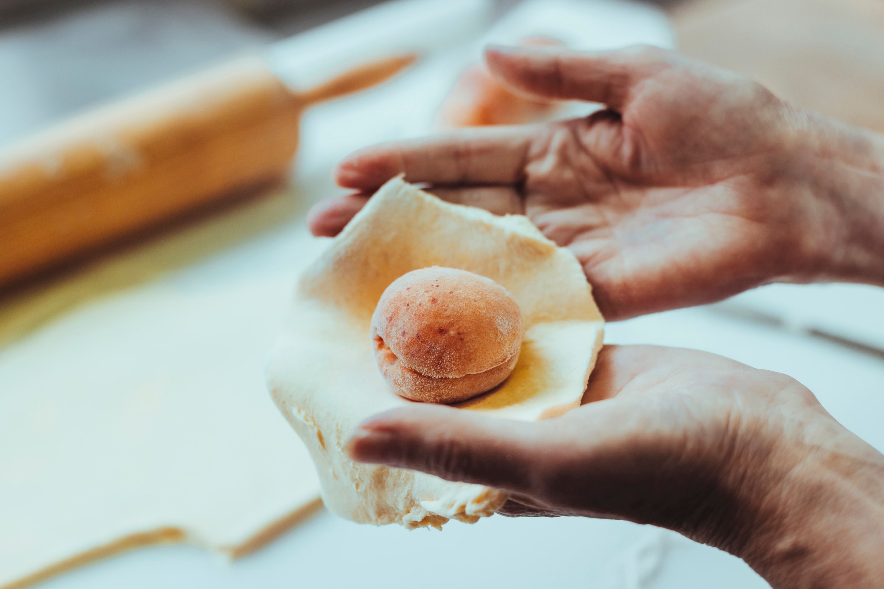Hands form a dough around an apricot.