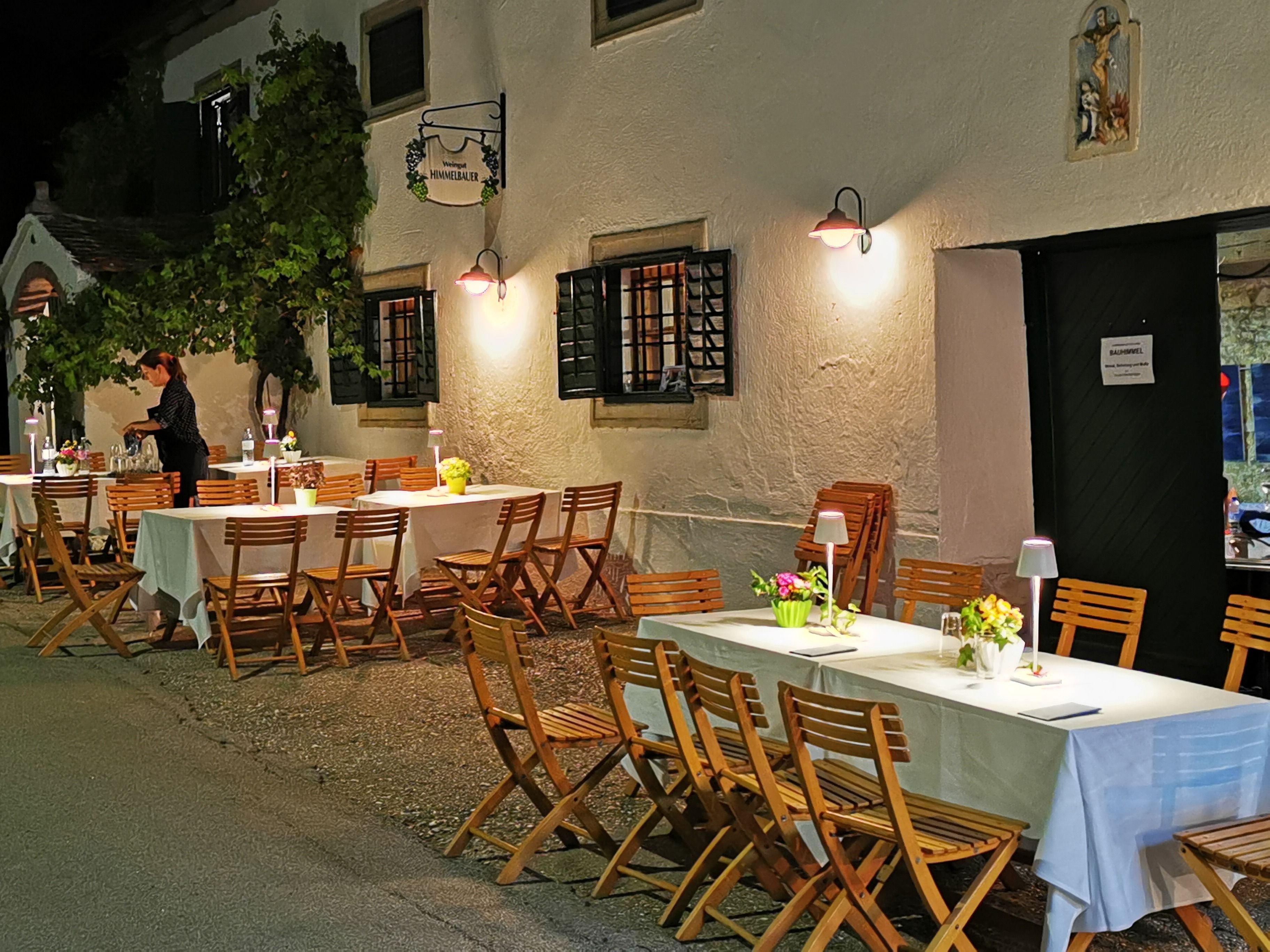 Outdoor area of a wine cellar with set tables and wooden chairs at night.