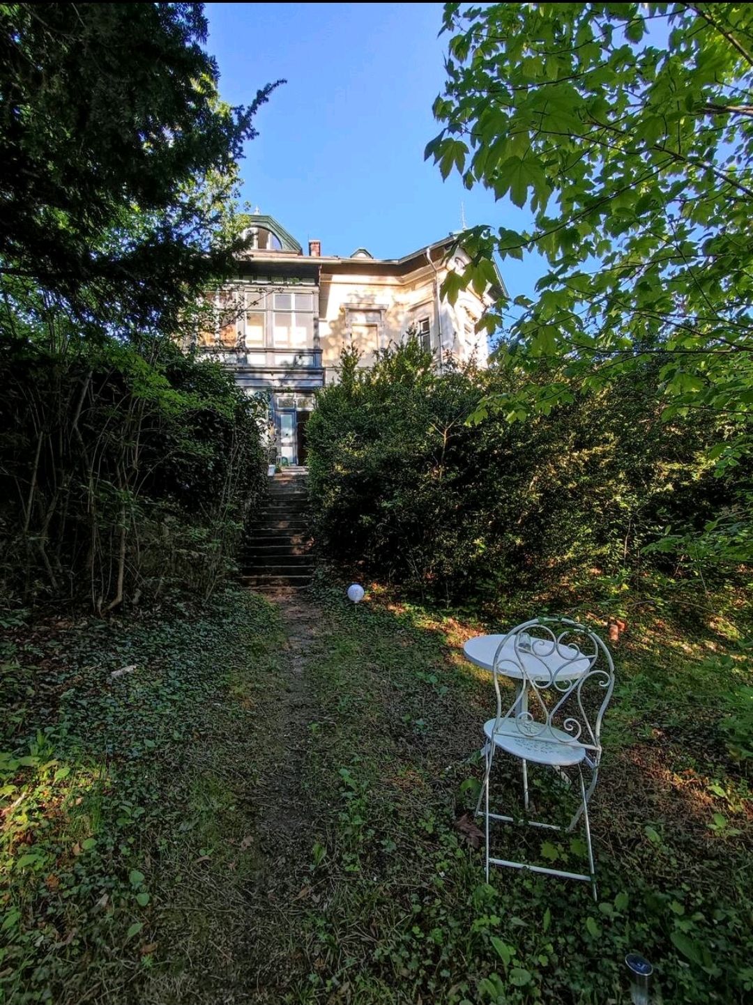 An old manor house with garden and garden furniture in the foreground.
