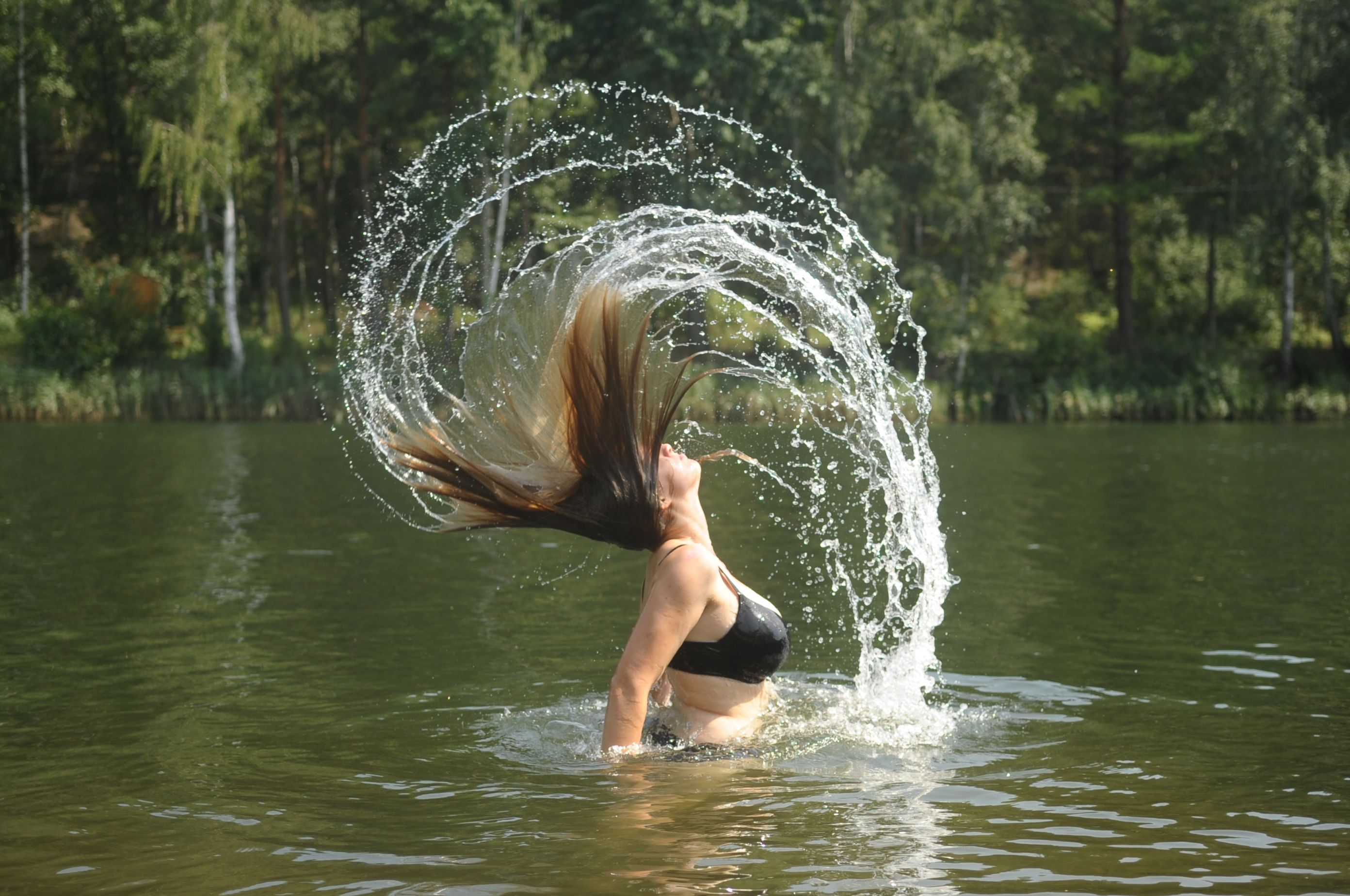 Woman throws her hair back in the water, creating a splash of water.