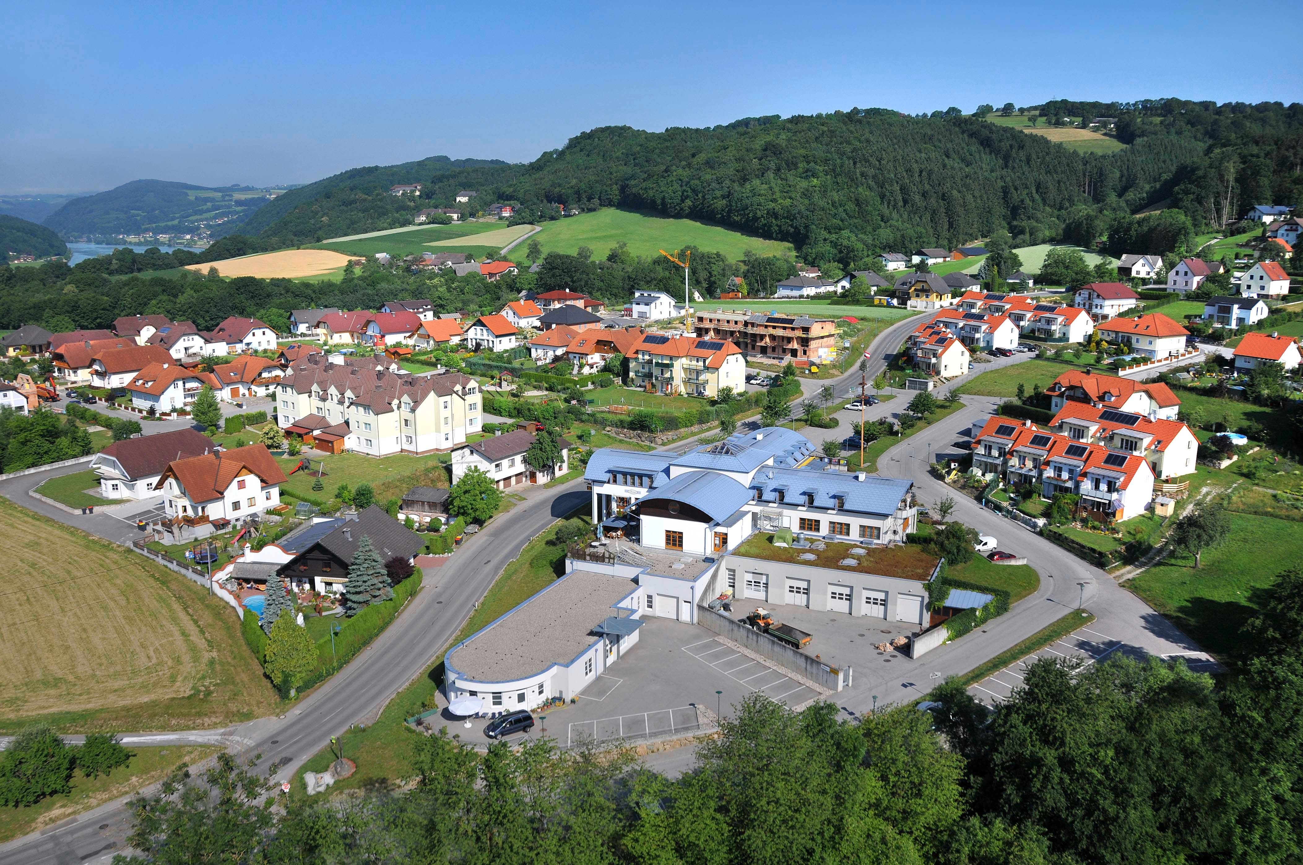 Aerial view of a village with community center and surrounding houses in a green hilly landscape.