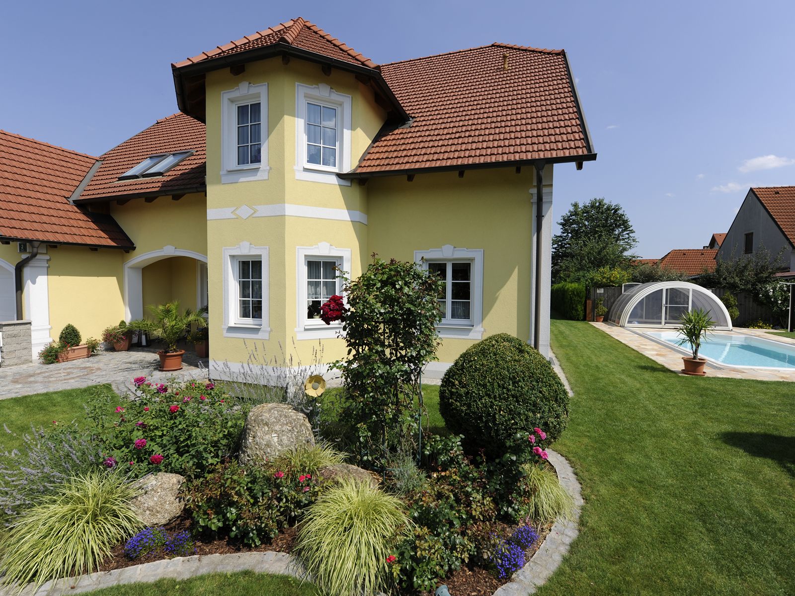 Yellow guest house with red roof, garden and pool.