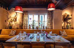 Cozy dining area with large windows, green upholstered furniture and plants, with a view of the countryside.
